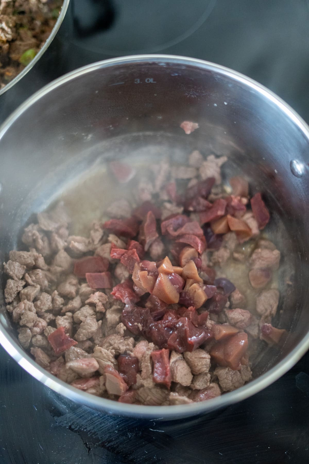 Cubed meat and organ pieces simmer in a stainless steel saucepan on the hob, steam rising—an irresistible lamb stew for dogs.