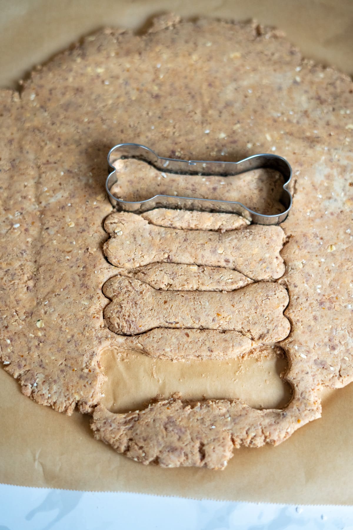 Rolled-out dough with a bone-shaped biscuit cutter cutting multiple bone-shaped pieces on baking paper.