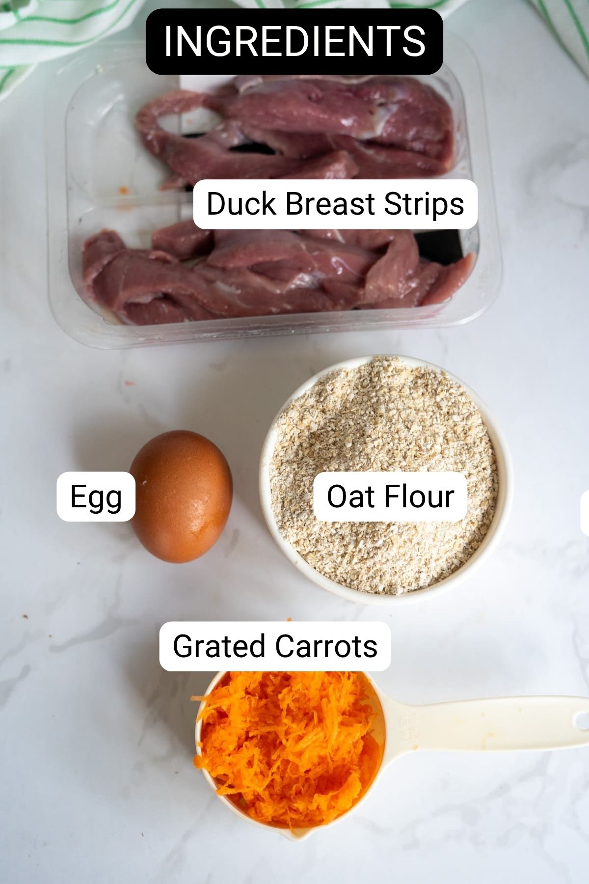 Duck breast strips, a whole egg, oat flour in a bowl, and grated carrots in a measuring jug displayed on a white surface—labelled as ingredients for homemade duck dog treats.