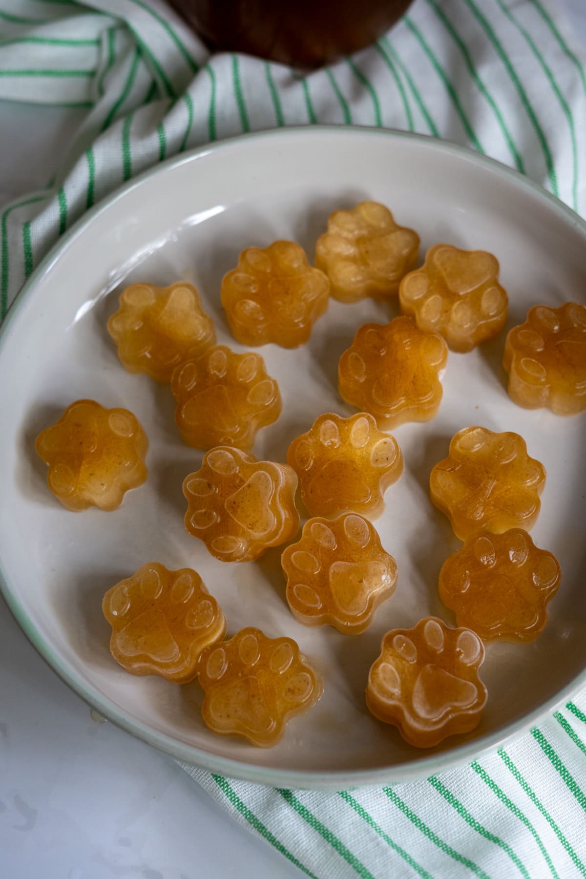 A white plate with several paw-shaped gummy treats made from beef bone broth for dogs sits on a white and green striped cloth.