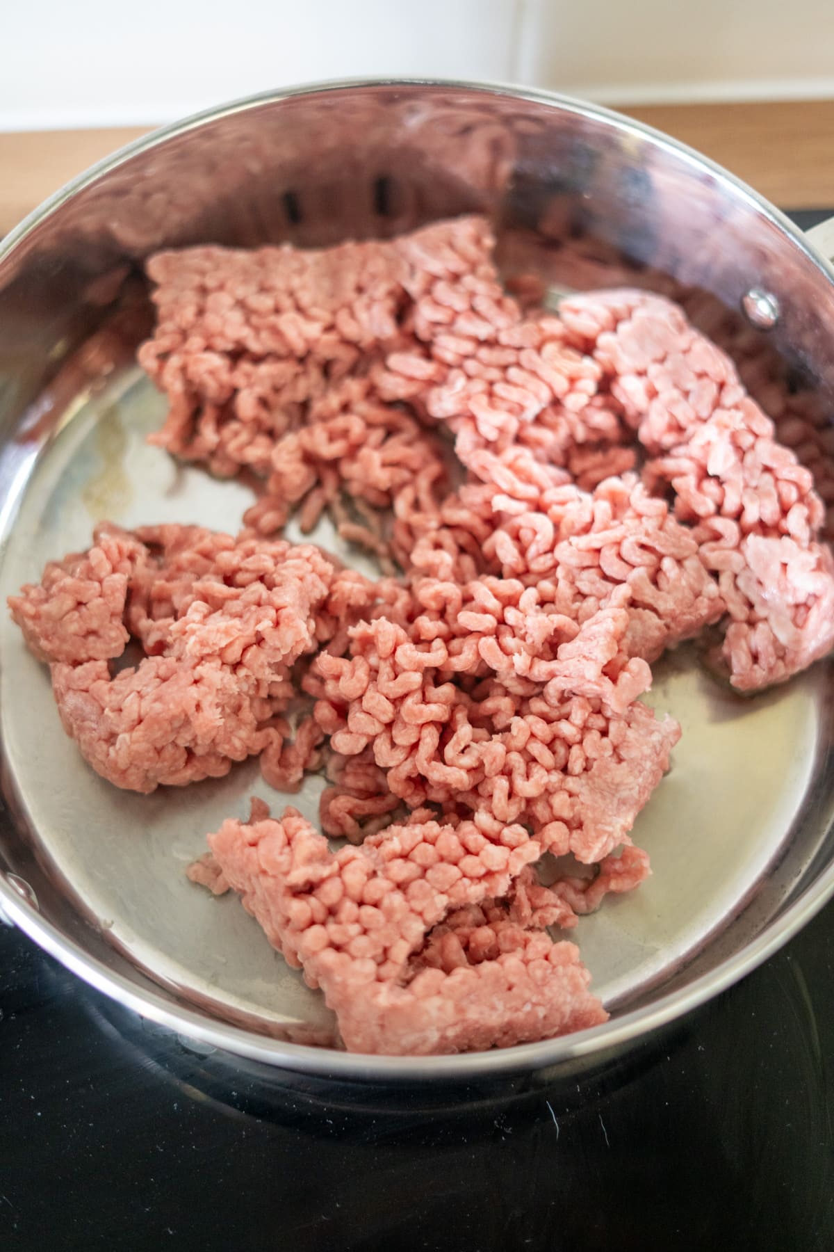 Raw minced beef in a stainless steel pan on a hob, ready to be cooked.