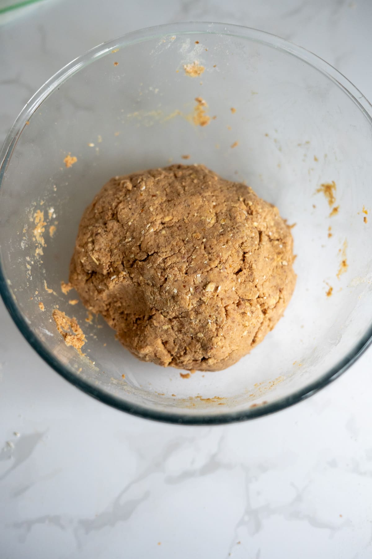 A ball of biscuit dough sits in a clear glass mixing bowl on a white marble worktop.