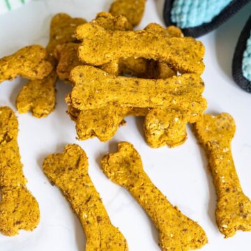 Bone-shaped dog biscuits arranged on a white surface with a blue and black oven glove partially visible in the background.