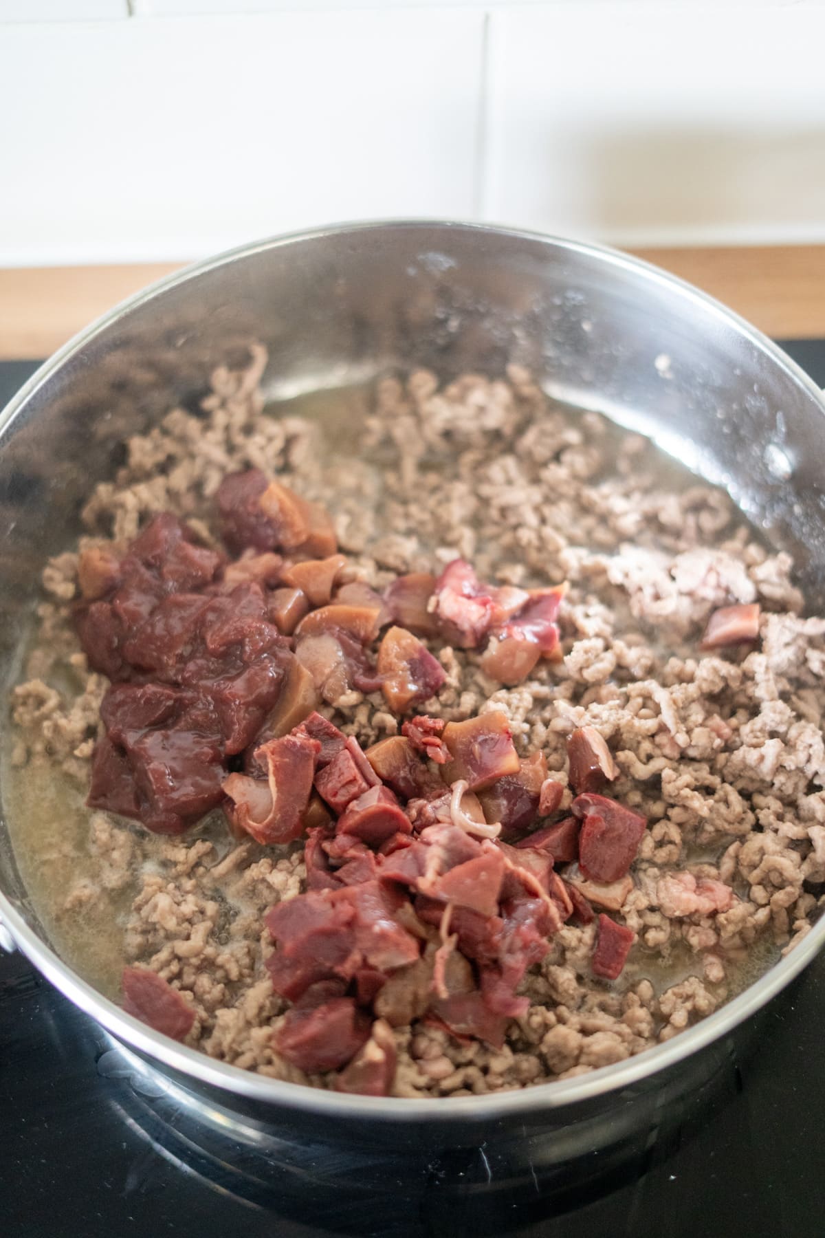 A stainless steel pan on a hob containing cooked minced meat and uncooked diced offal.
