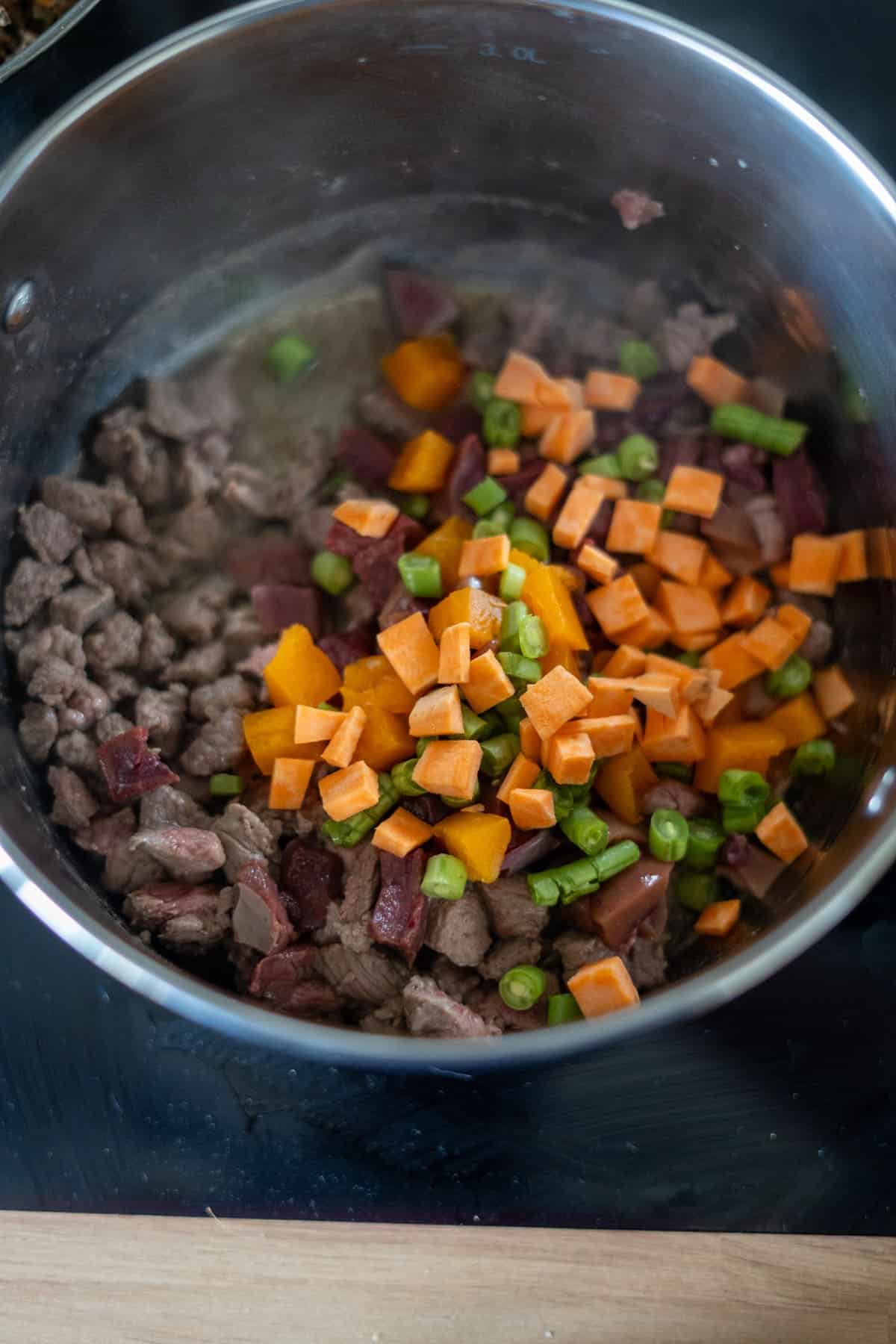 Lamb stew for dogs with diced beef, carrots, peas, and sweet potatoes simmering in a stainless steel pot on the hob.