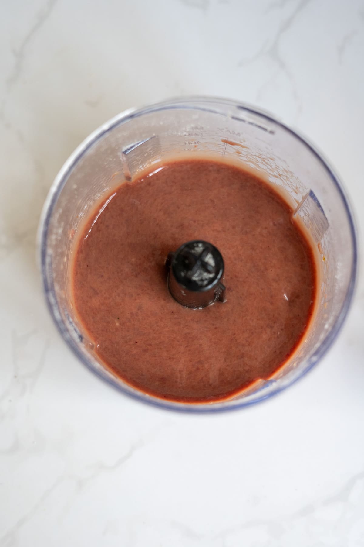 A blender jug filled with a reddish-brown liquid mixture for homemade duck dog treats sits on a white marble surface.