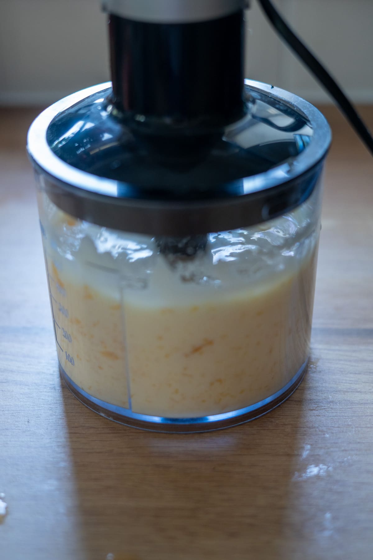 A food processor blending a creamy yellow mixture on a wooden worktop.