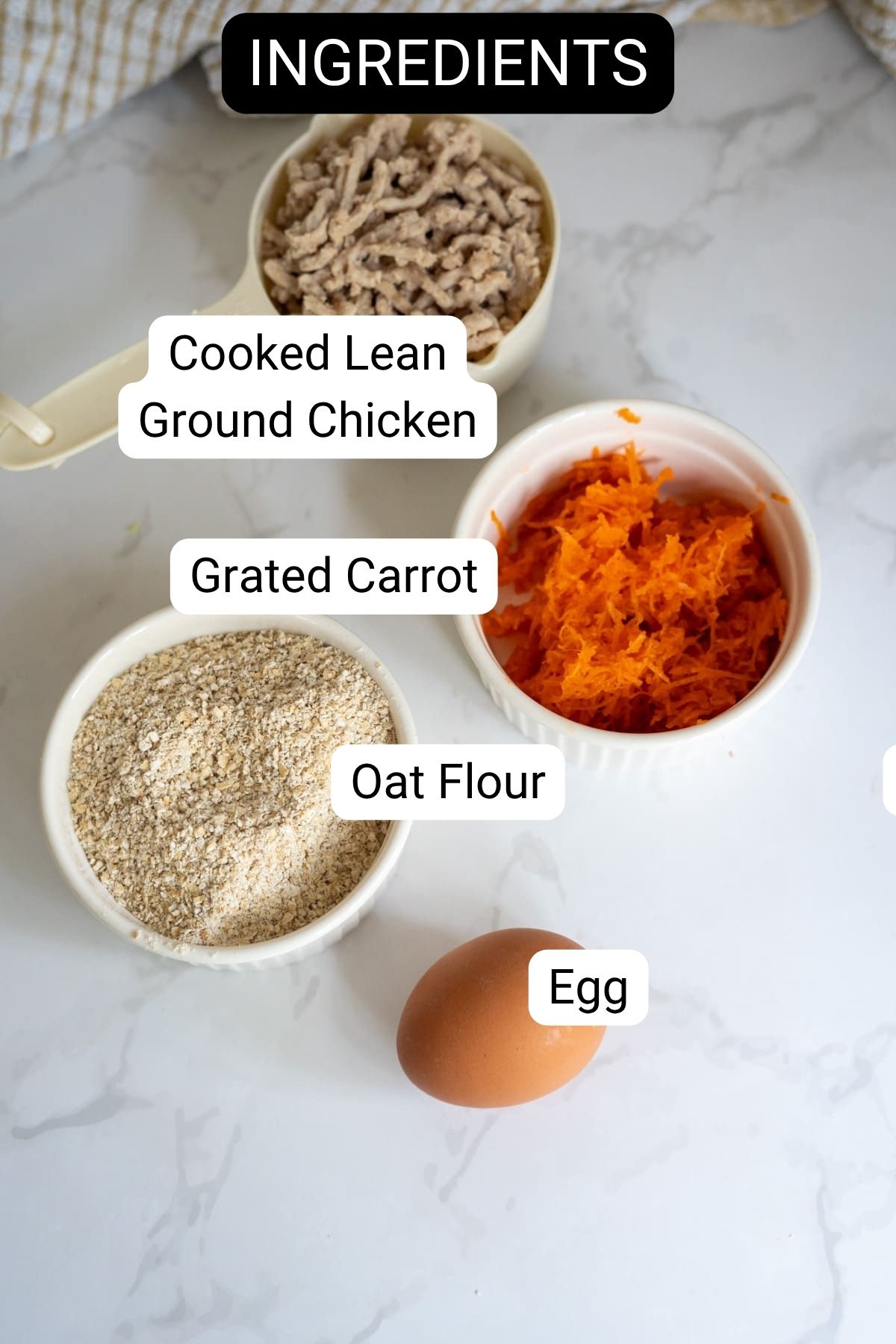 Four labelled ingredients on a white surface: cooked lean minced chicken, grated carrot, oat flour, and an egg.