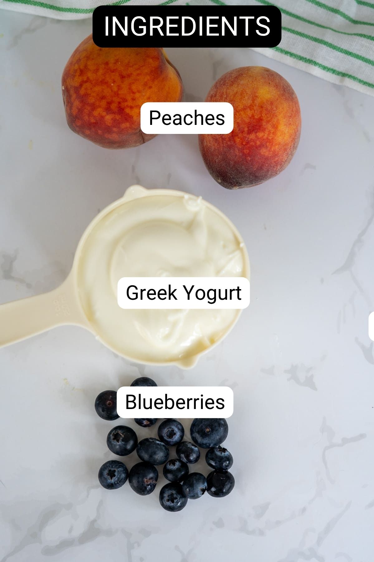 Overhead view of two peaches, a pot of Greek yoghurt, and a handful of blueberries labelled as ingredients on a marble surface.