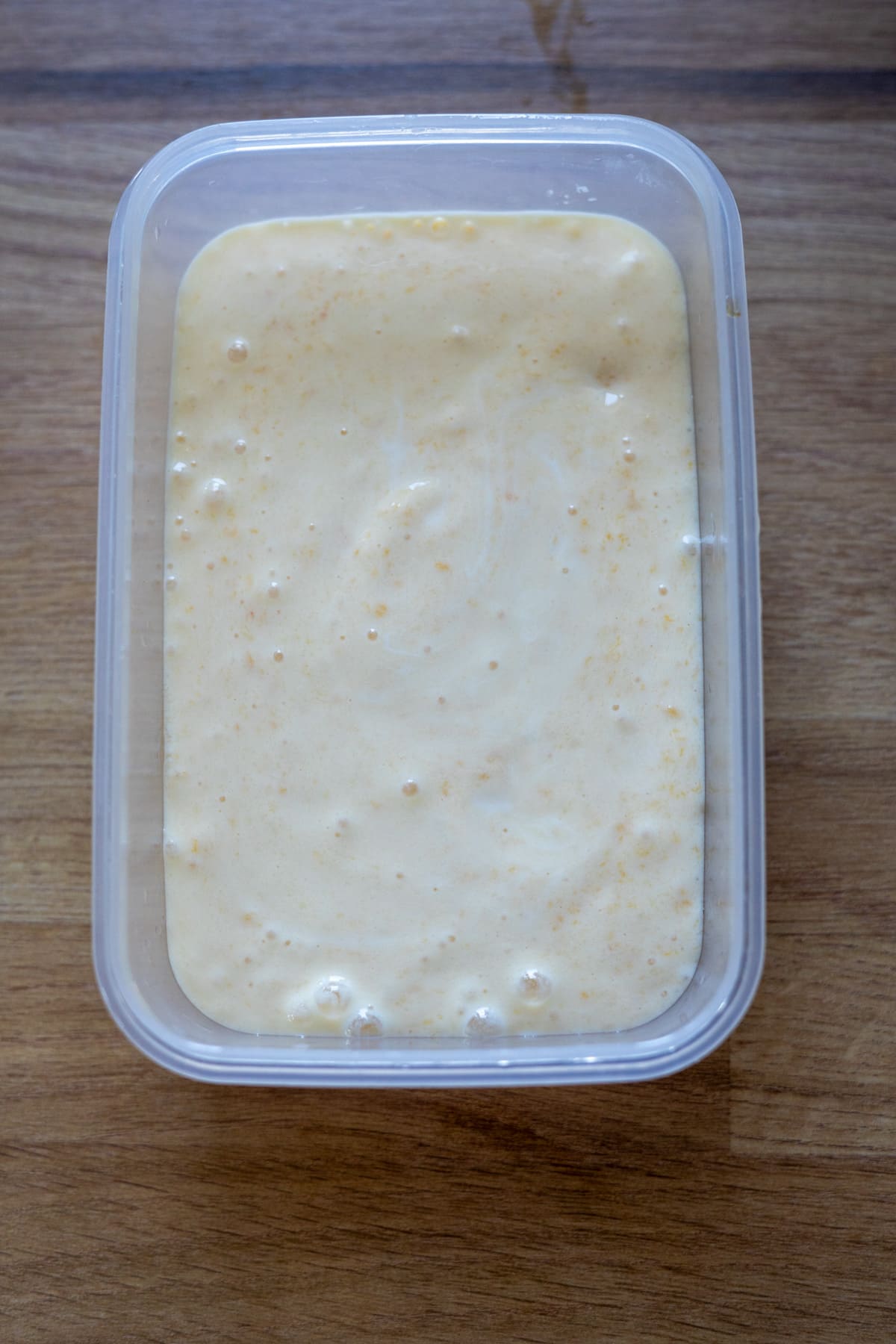 A rectangular plastic container filled with a thick, pale yellow creamy mixture sits on a wooden surface.