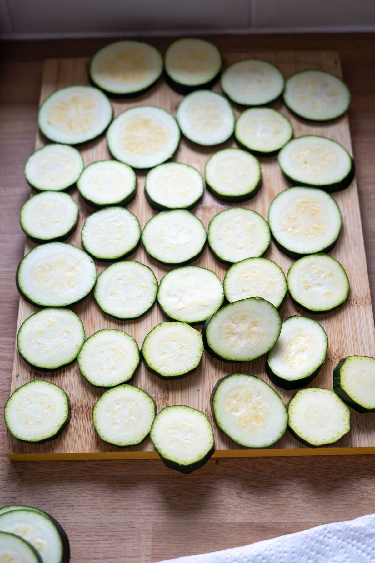 Sliced courgette pieces arranged in a single layer on a wooden chopping board.