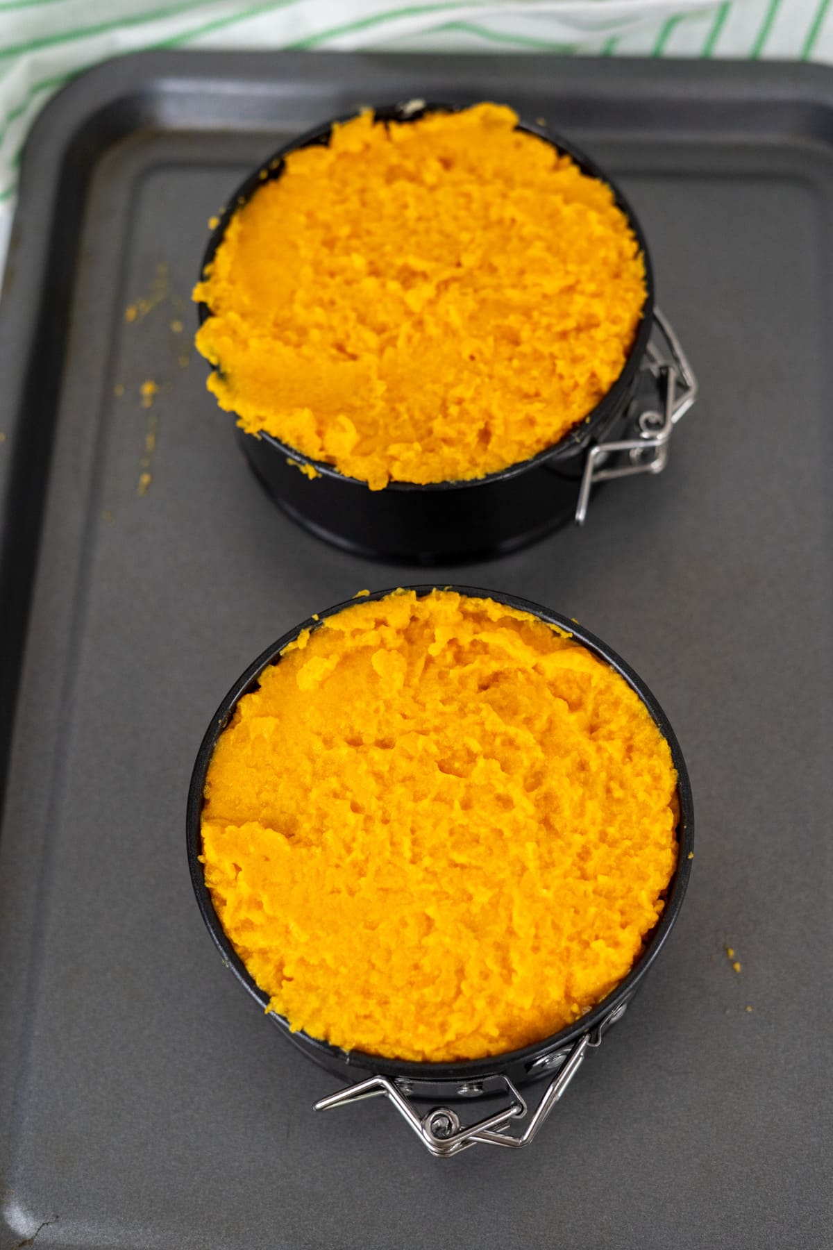 Two small round baking tins filled with orange mashed mixture, placed on a metal baking tray.