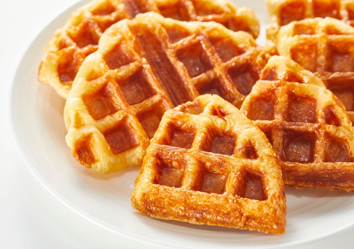 A white plate with several golden-brown, heart-shaped waffle pieces arranged closely together.