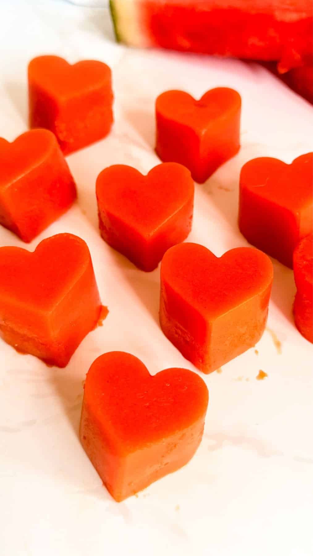 Nine heart-shaped watermelon pieces are arranged on a white surface.