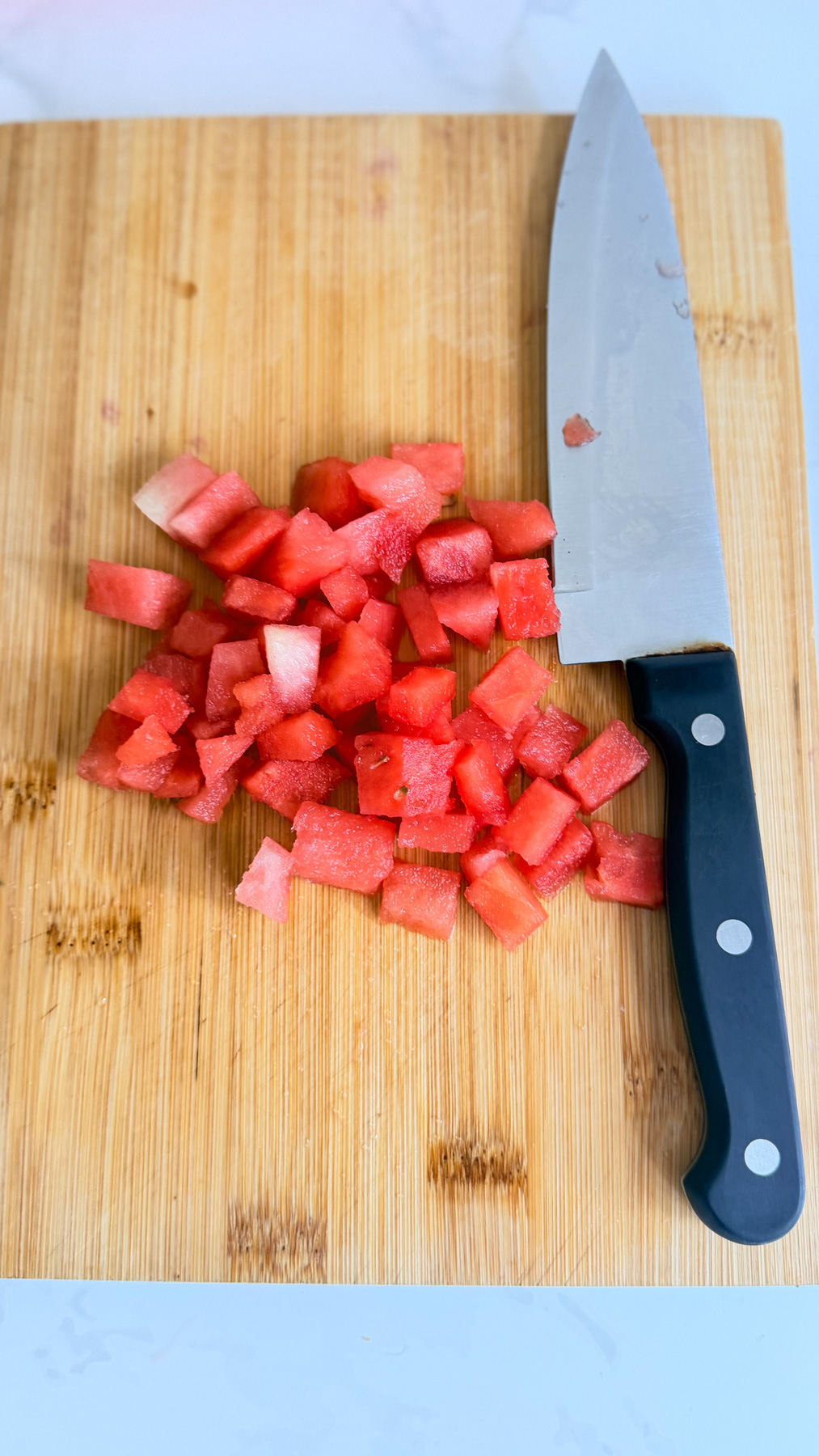 Diced watermelon pieces and a kitchen knife are placed on a wooden chopping board.