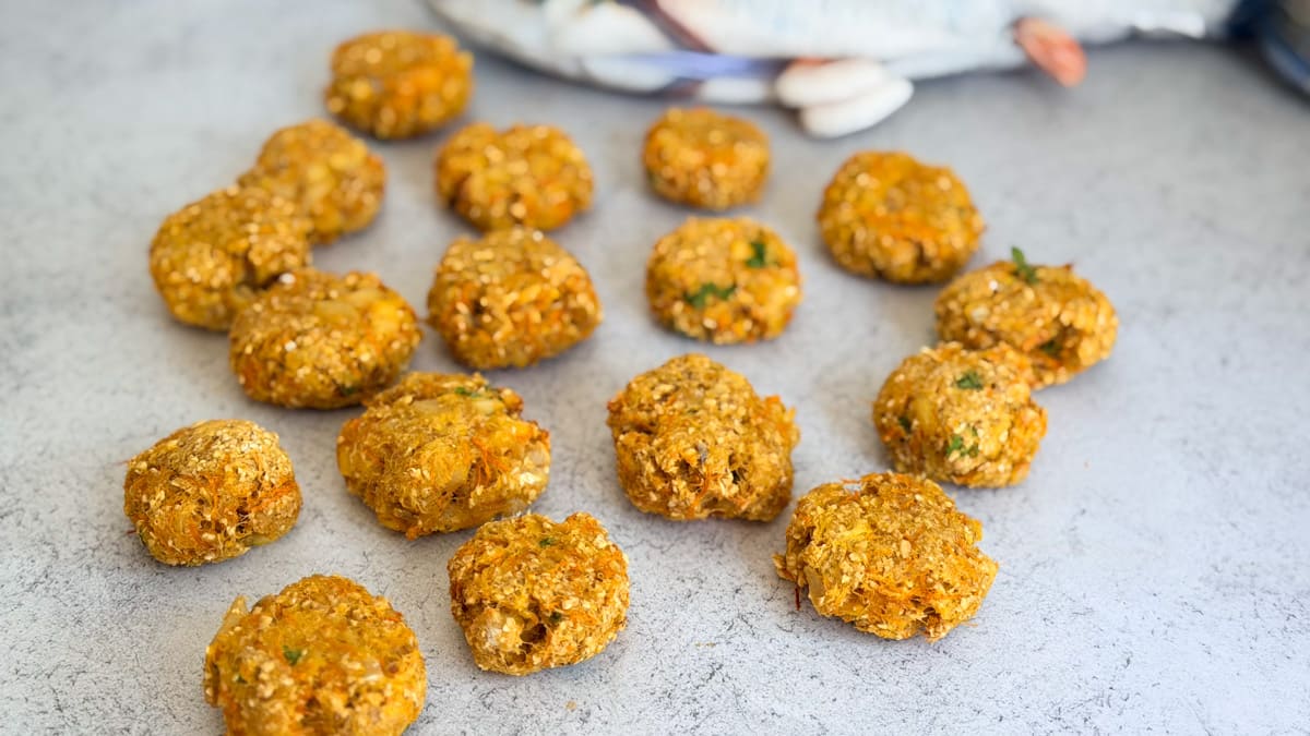 Several round, golden-brown baked patties are arranged on a light surface, with a blurred background containing a blue and white object.