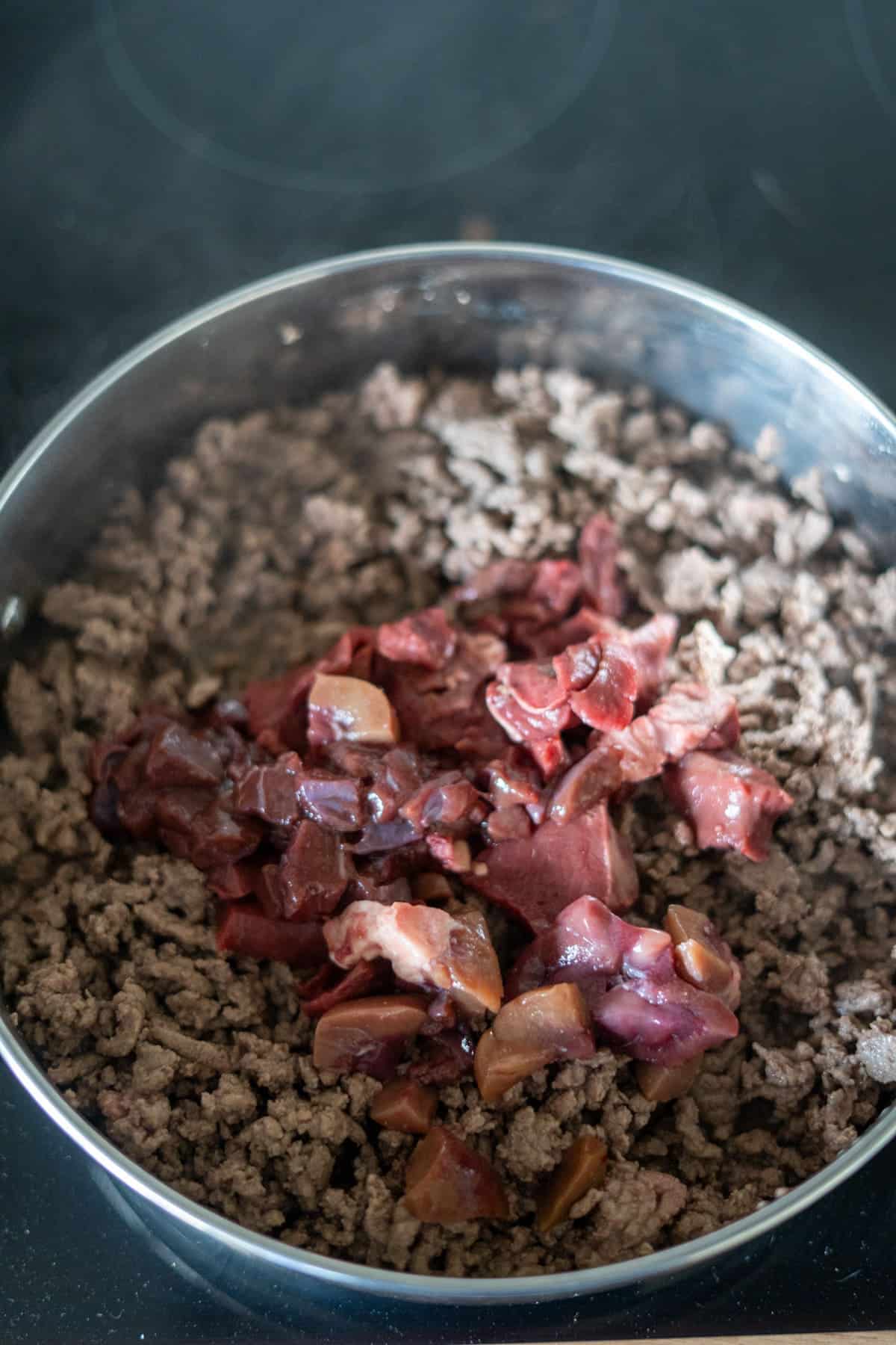 Minced beef cooking in a frying pan with a portion of raw chopped liver added on top, creating a wholesome beef dog food recipe.