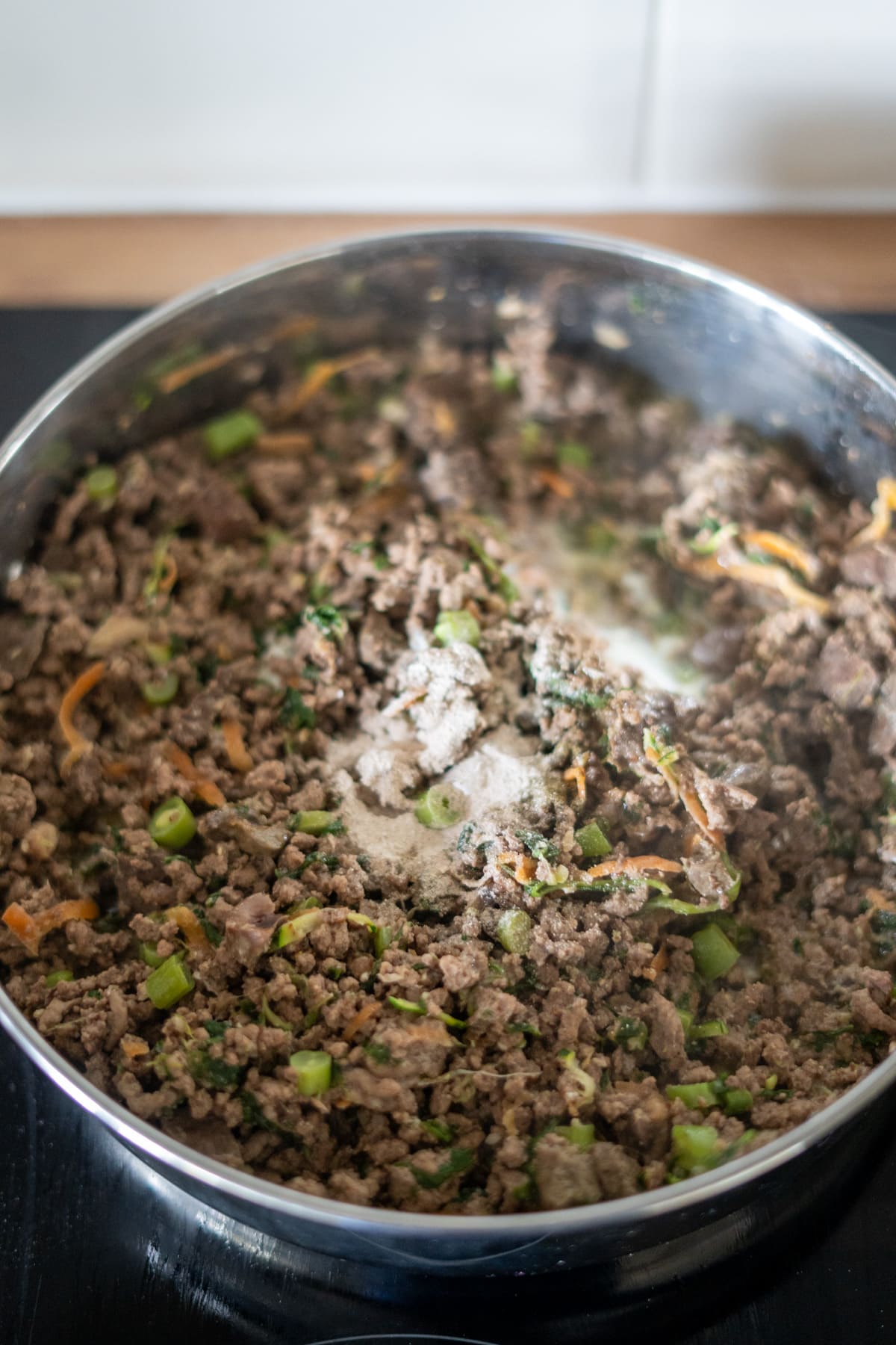 Minced beef cooked with chopped vegetables and seasonings in a stainless steel pan—an easy beef dog food recipe for your furry friend.
