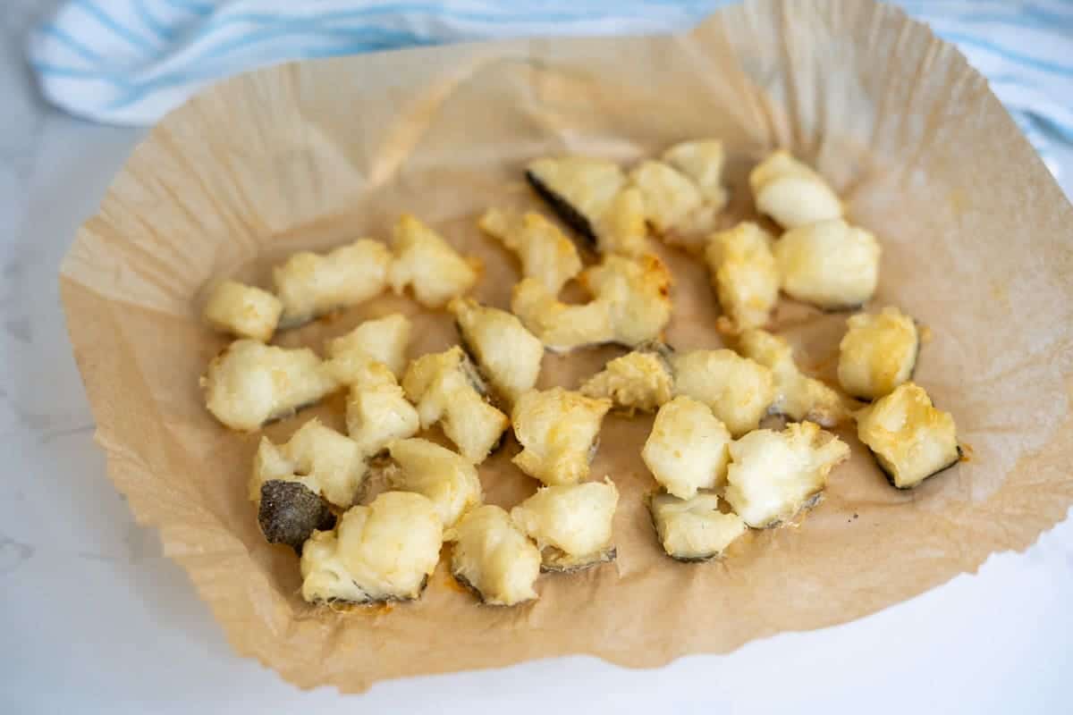 Battered and fried cod bites for dogs arranged on a sheet of brown greaseproof paper.