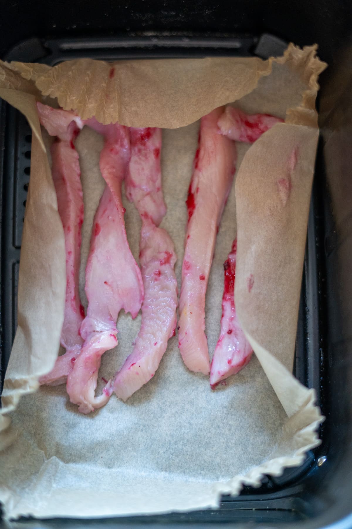 Raw fish fillets placed on baking parchment inside an air fryer basket, ready for cooking—much like preparing turkey jerky for dogs using this convenient method.