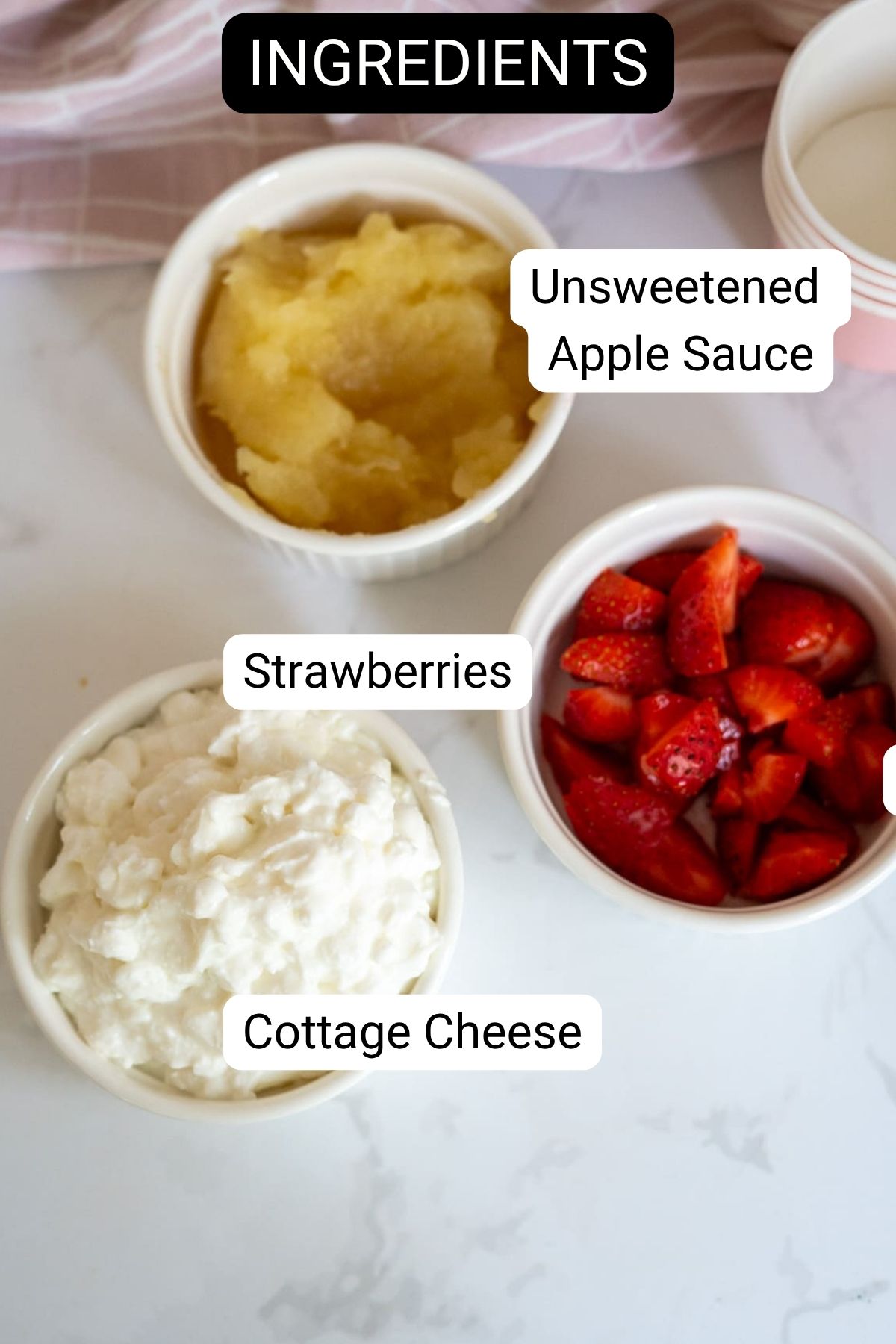 Three bowls on a white worktop containing unsweetened apple purée, chopped strawberries, and cottage cheese—perfect ingredients for homemade apple and strawberry dog ice cream—labelled as ingredients.
