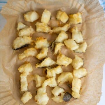 Battered and fried fish pieces arranged on greaseproof paper.