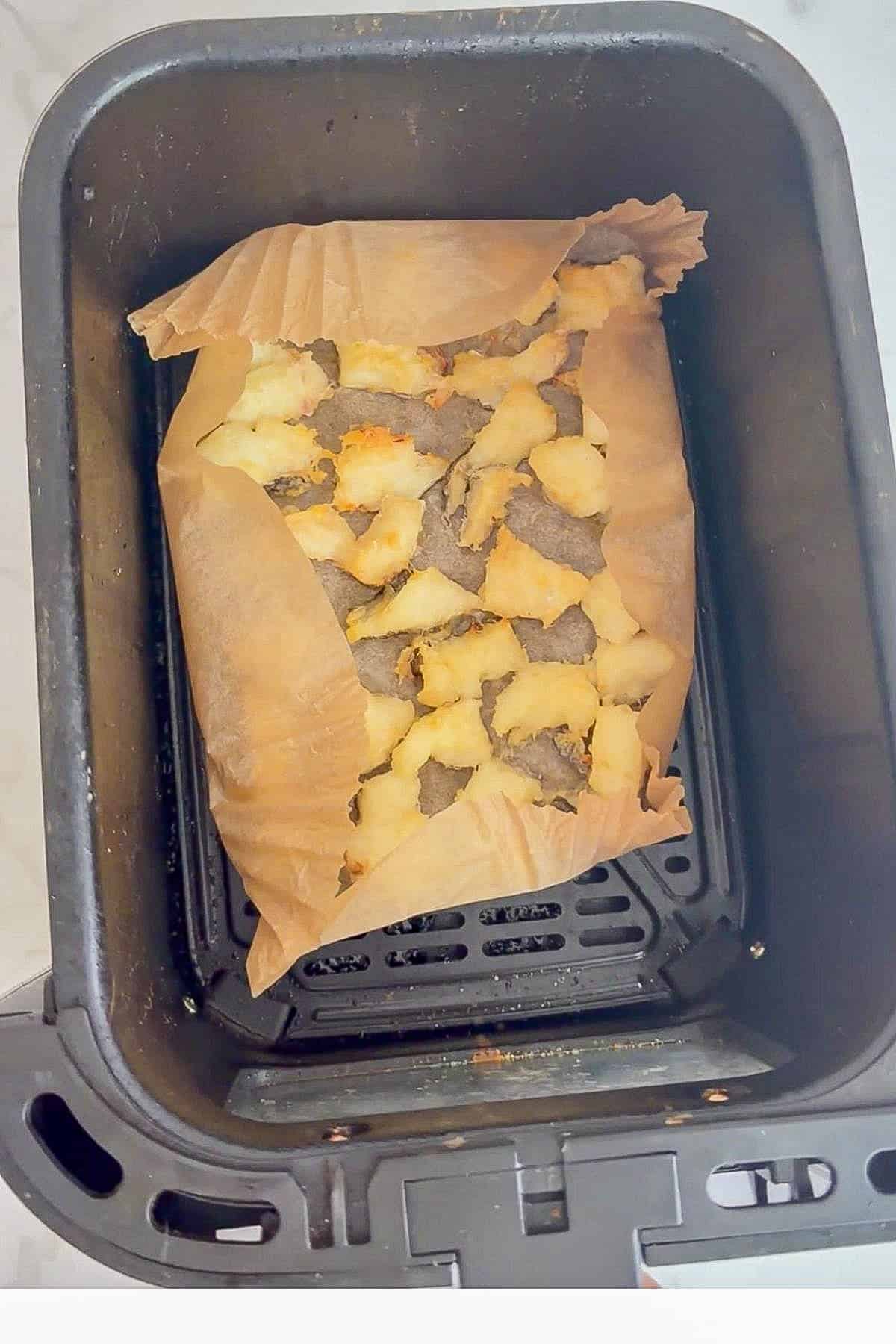 A batch of unevenly cooked biscuits sits on baking parchment inside an air fryer basket, resembling homemade cod bites for dogs.