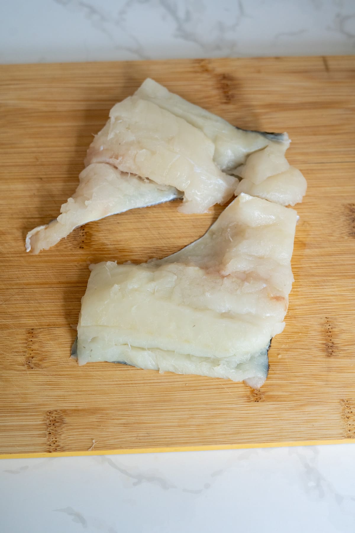 Two raw fish fillets with skin on, placed on a wooden chopping board, perfect for preparing healthy cod bites for dogs.
