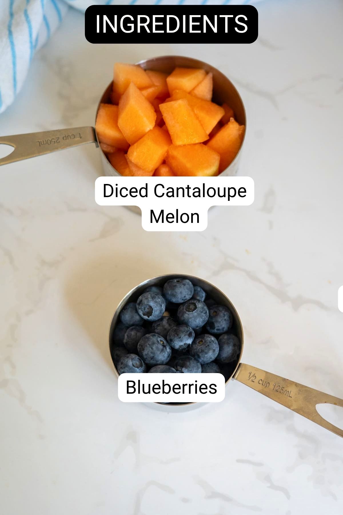 Two measuring jugs on a white surface, one filled with diced cantaloupe melon, the other with blueberries—perfect ingredients for homemade frozen cantaloupe and blueberry dog treats. Labels clearly indicate each ingredient.