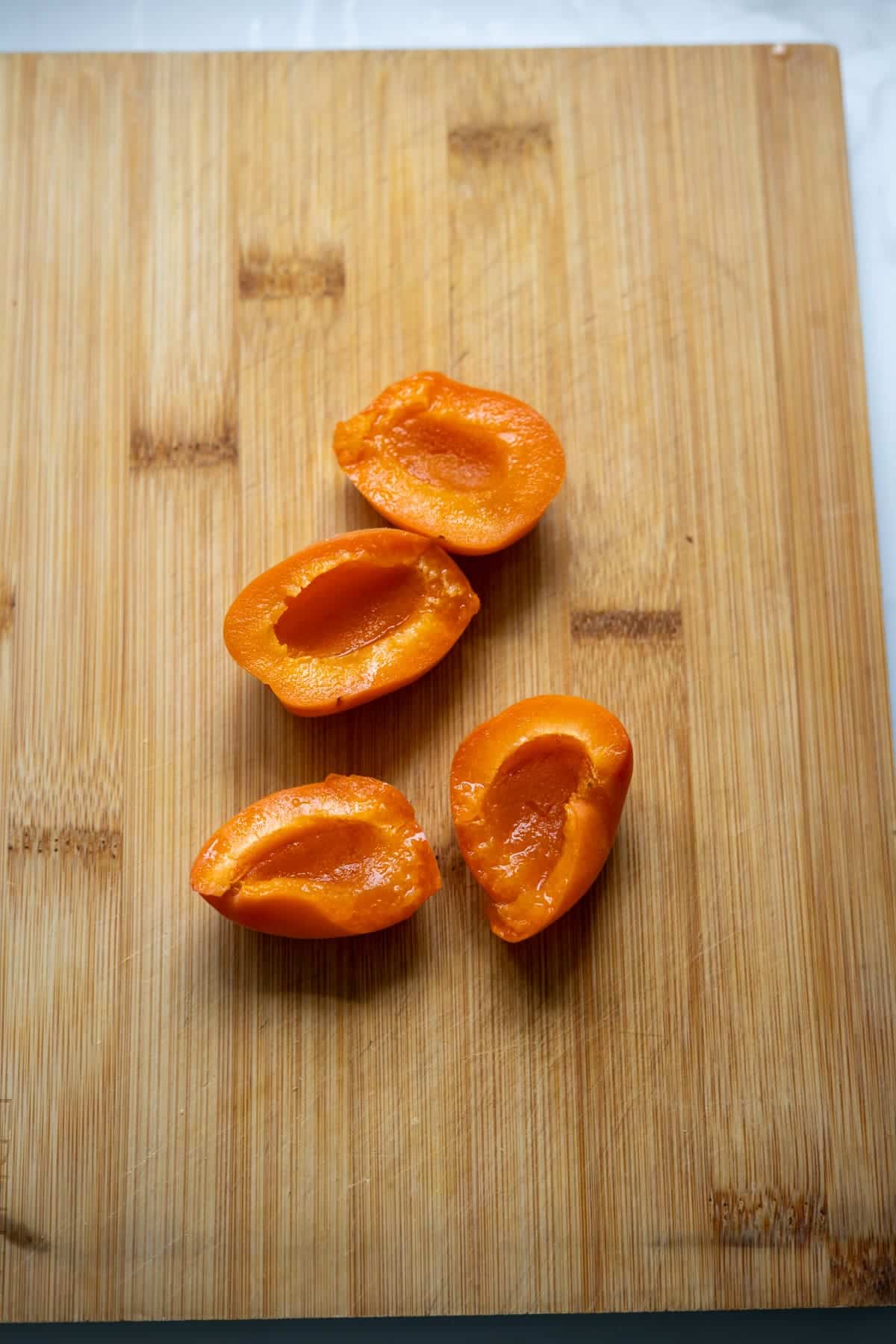 Four apricot halves are placed on a wooden chopping board.