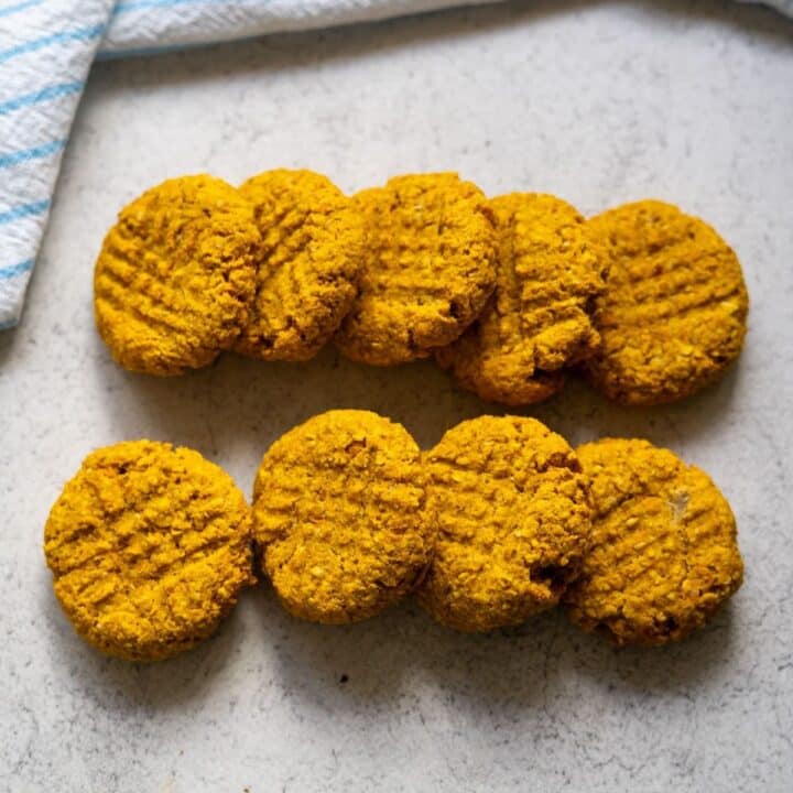 Eight round, golden-brown biscuits with a criss-cross fork pattern are arranged in two rows on a light-coloured surface.