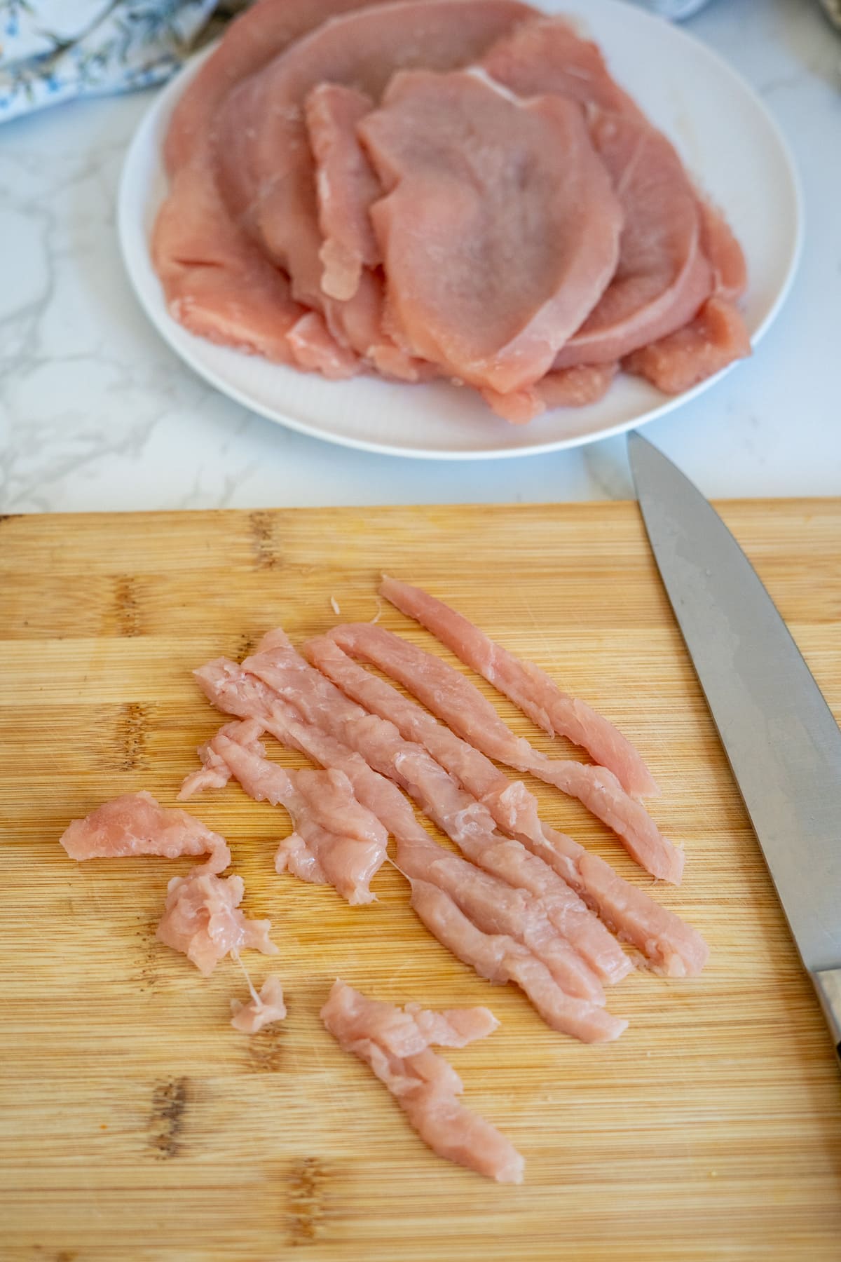 Raw turkey slices on a plate and thin turkey strips on a wooden chopping board, next to a kitchen knife—perfect ingredients for making wholesome turkey jerky for dogs.