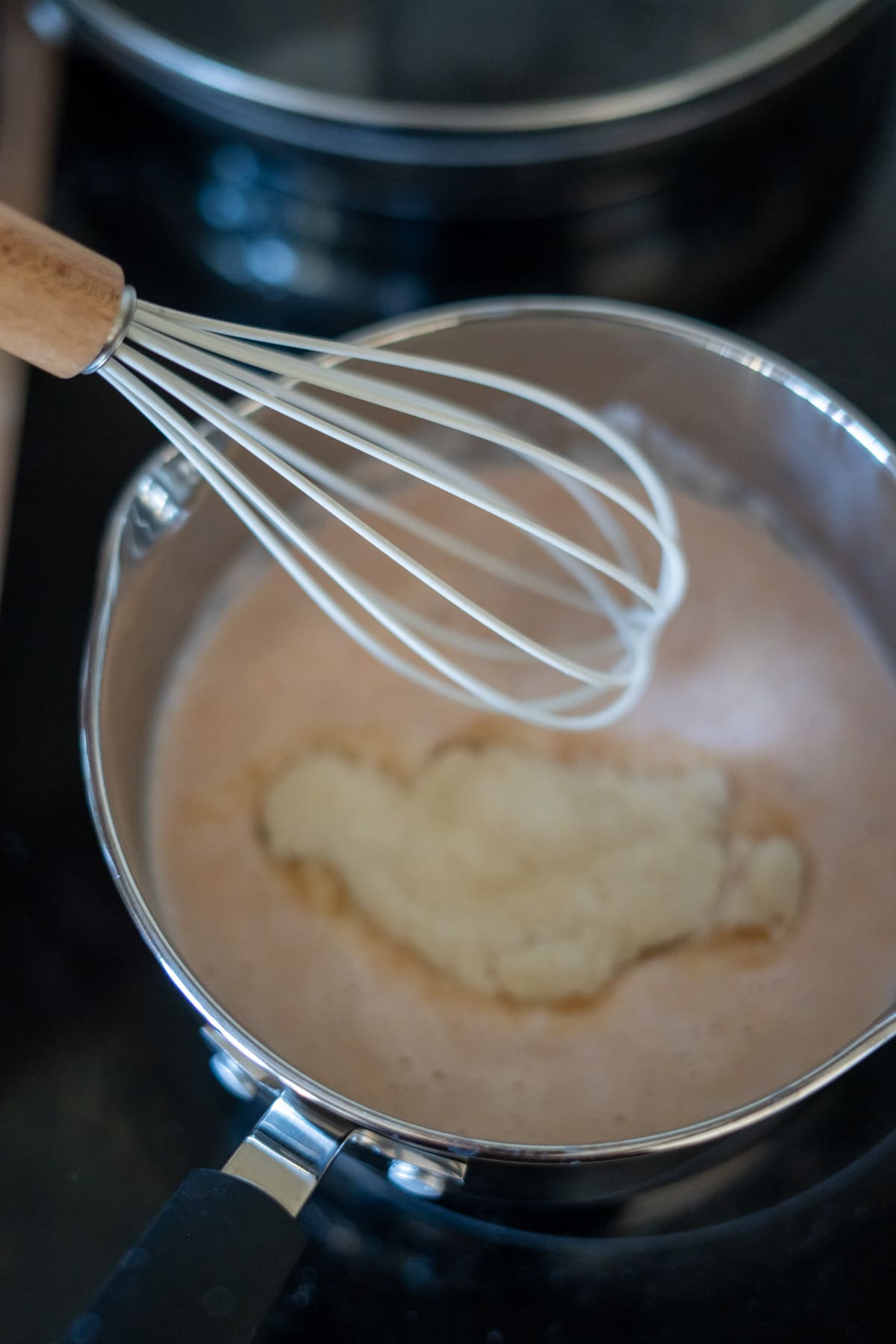 A metal saucepan with a light brown mixture and a clump of flour being whisked on a hob, perfect for preparing savoury bases like salmon bone broth gummies.
