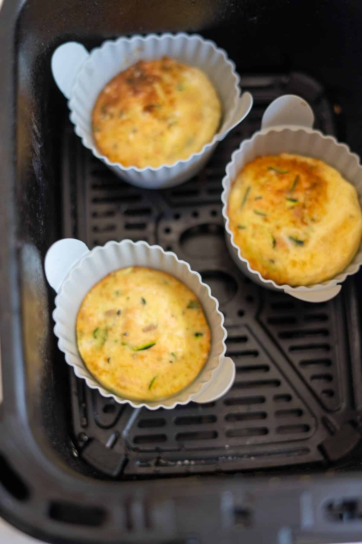 Three cooked egg bites in silicone cups sit inside an air fryer basket, reminiscent of a mini Air Fryer Salmon Dog Frittata.