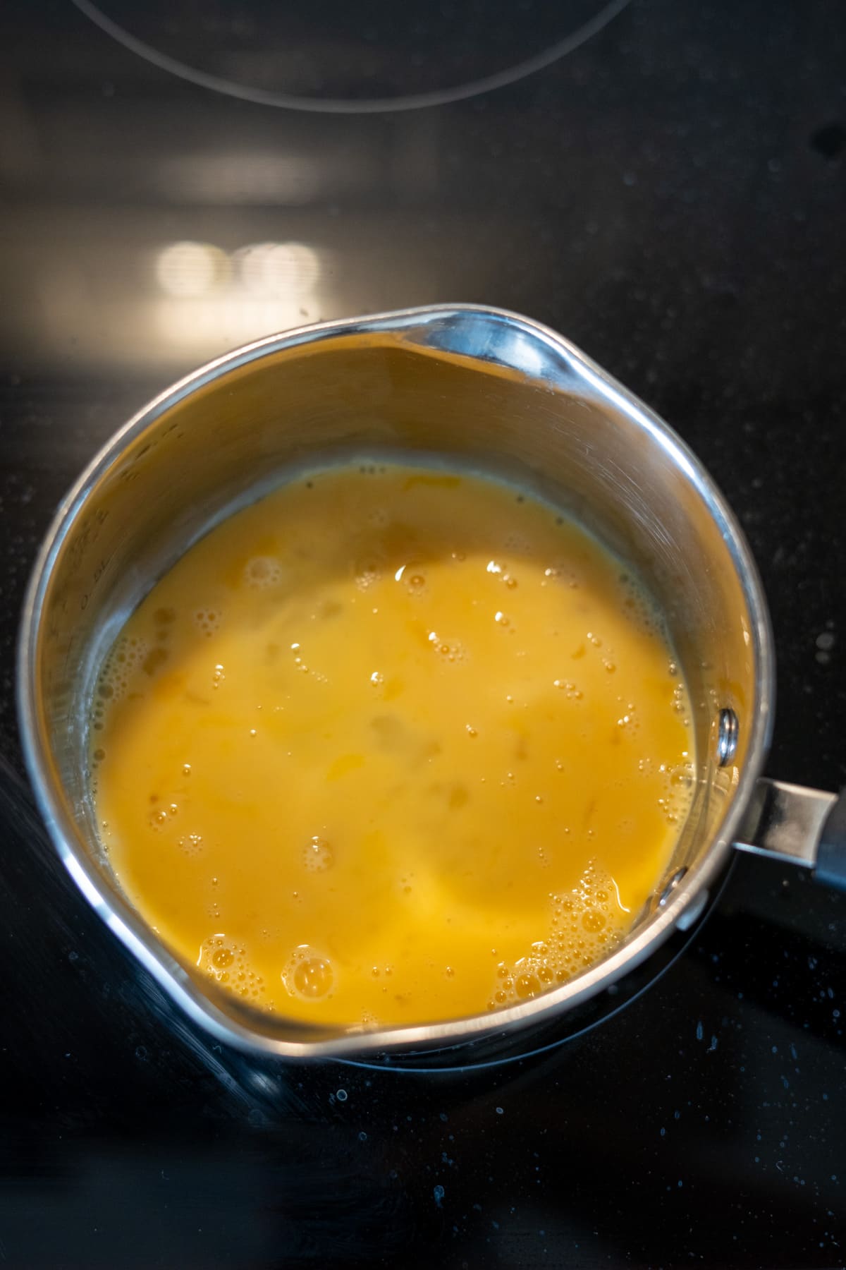 A stainless steel saucepan containing scrambled eggs for dogs, sitting on a black hob.
