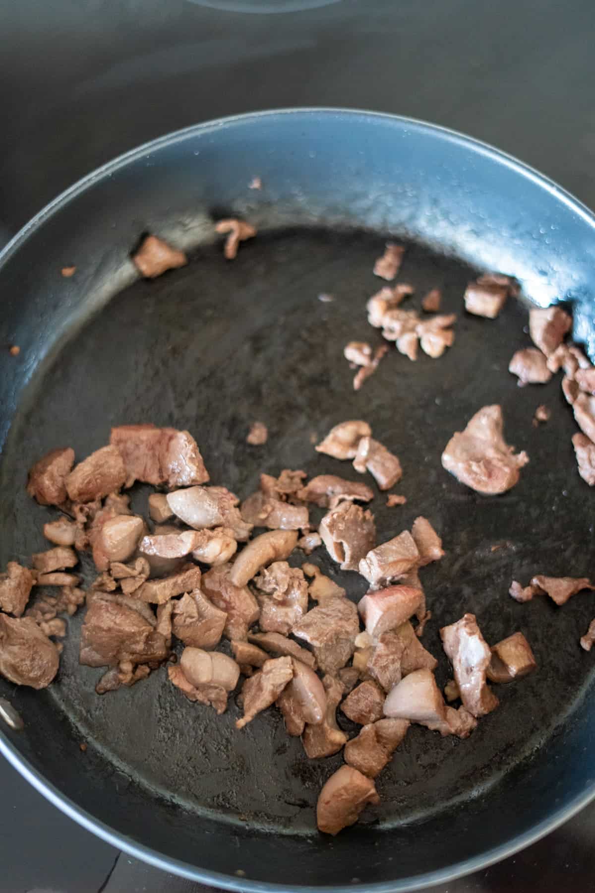 Chopped pieces of cooked meat scattered in a non-stick frying pan on a hob.