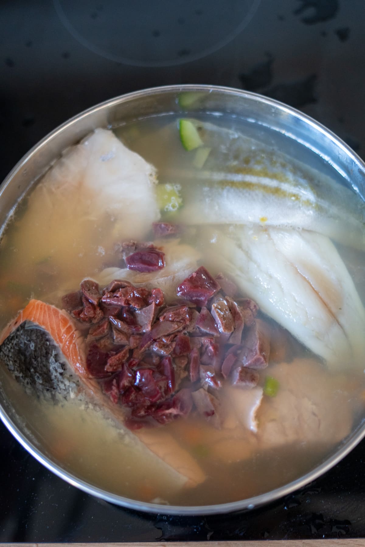A pot of fish stew for dogs featuring tender fish fillets, chopped dried jujubes, and fresh vegetables cooking in a savoury broth on the hob.