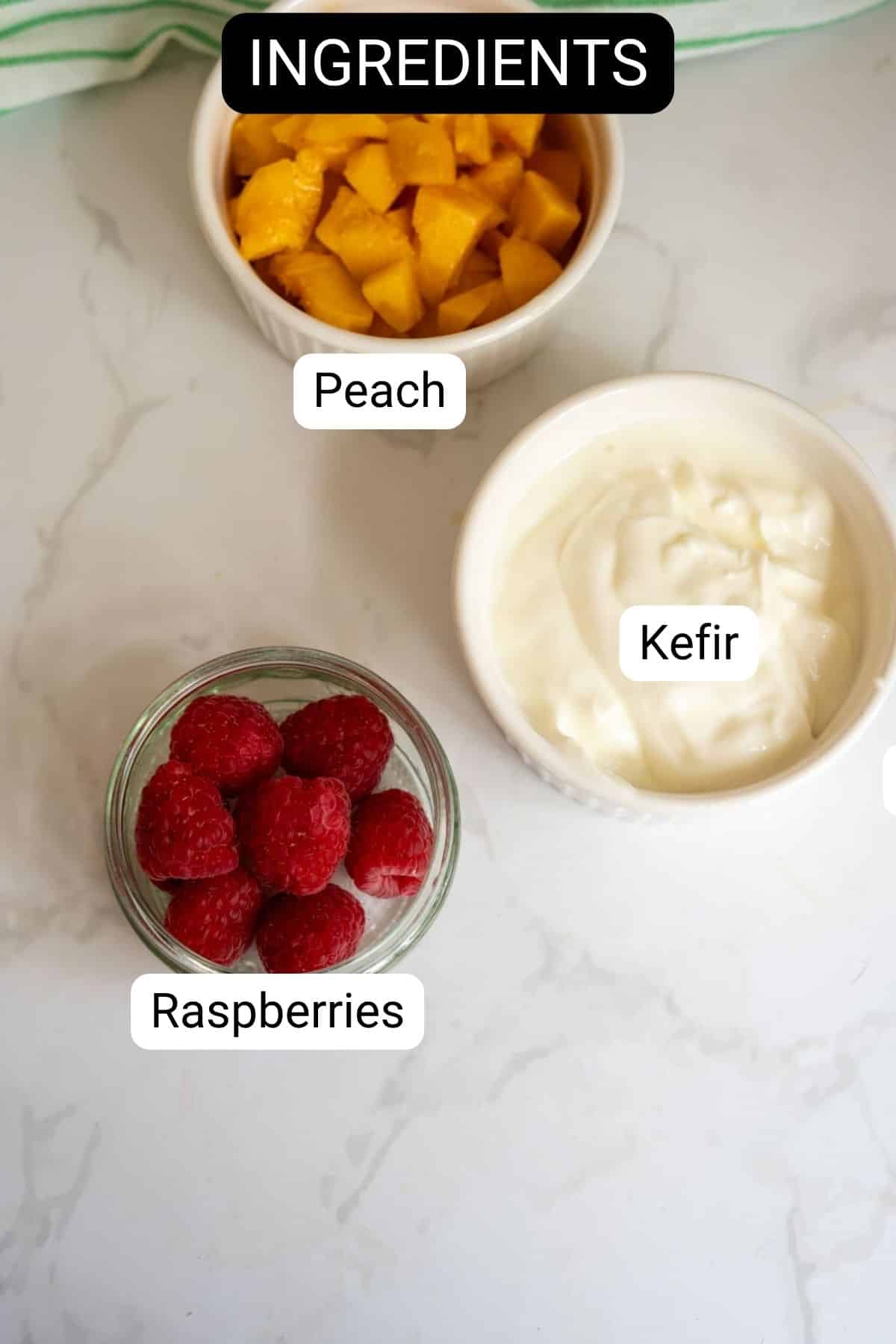 Three bowls on a white surface containing diced peach, raspberries, and kefir—perfect ingredients for Frozen Peach Raspberry Dog Treats—each labelled with its name. The word “INGREDIENTS” appears at the top of the image.