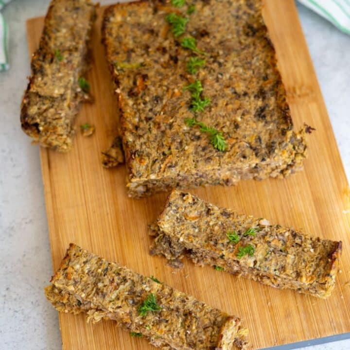 A rectangular loaf with visible vegetables and herbs, partially sliced, is displayed on a wooden chopping board.