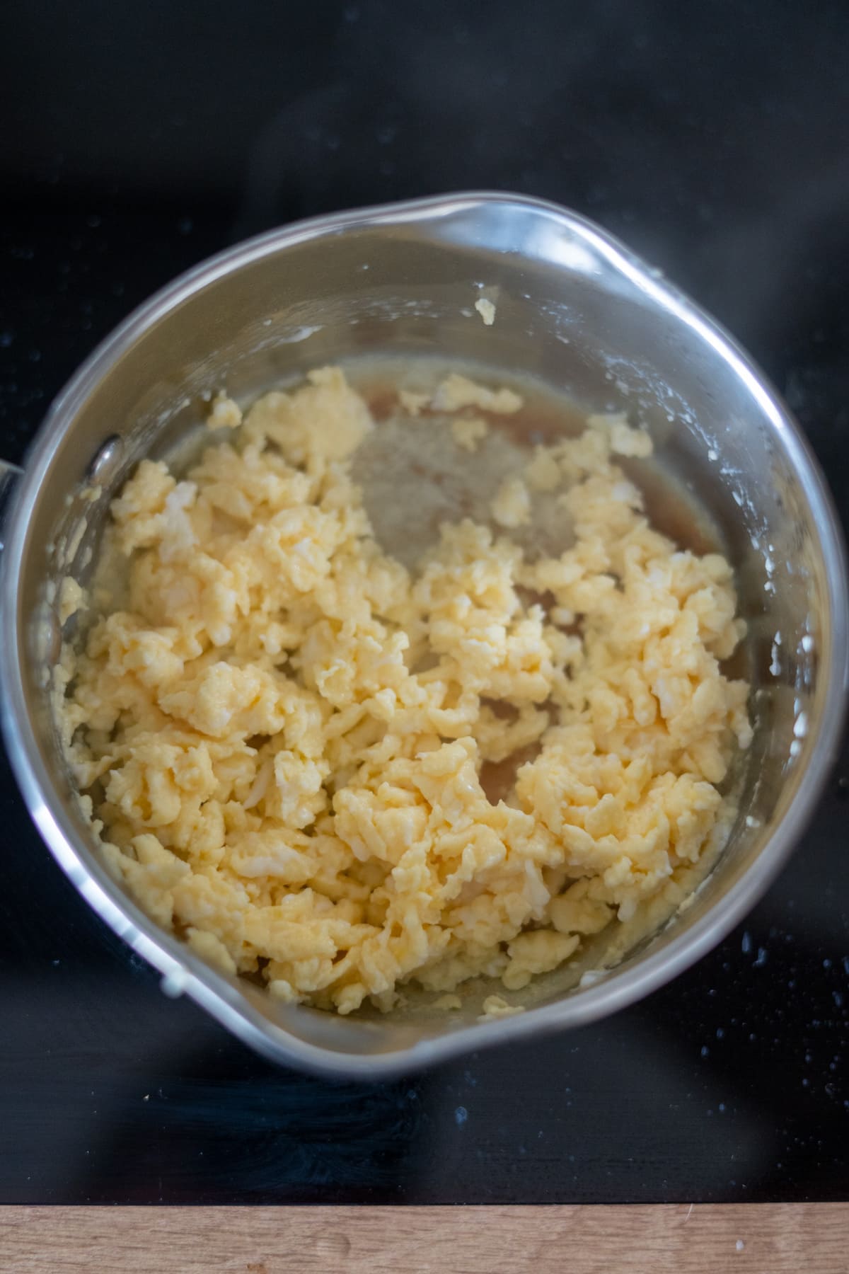 Scrambled eggs for dogs cooking in a stainless steel saucepan on a black hob, with some steam rising from the saucepan.
