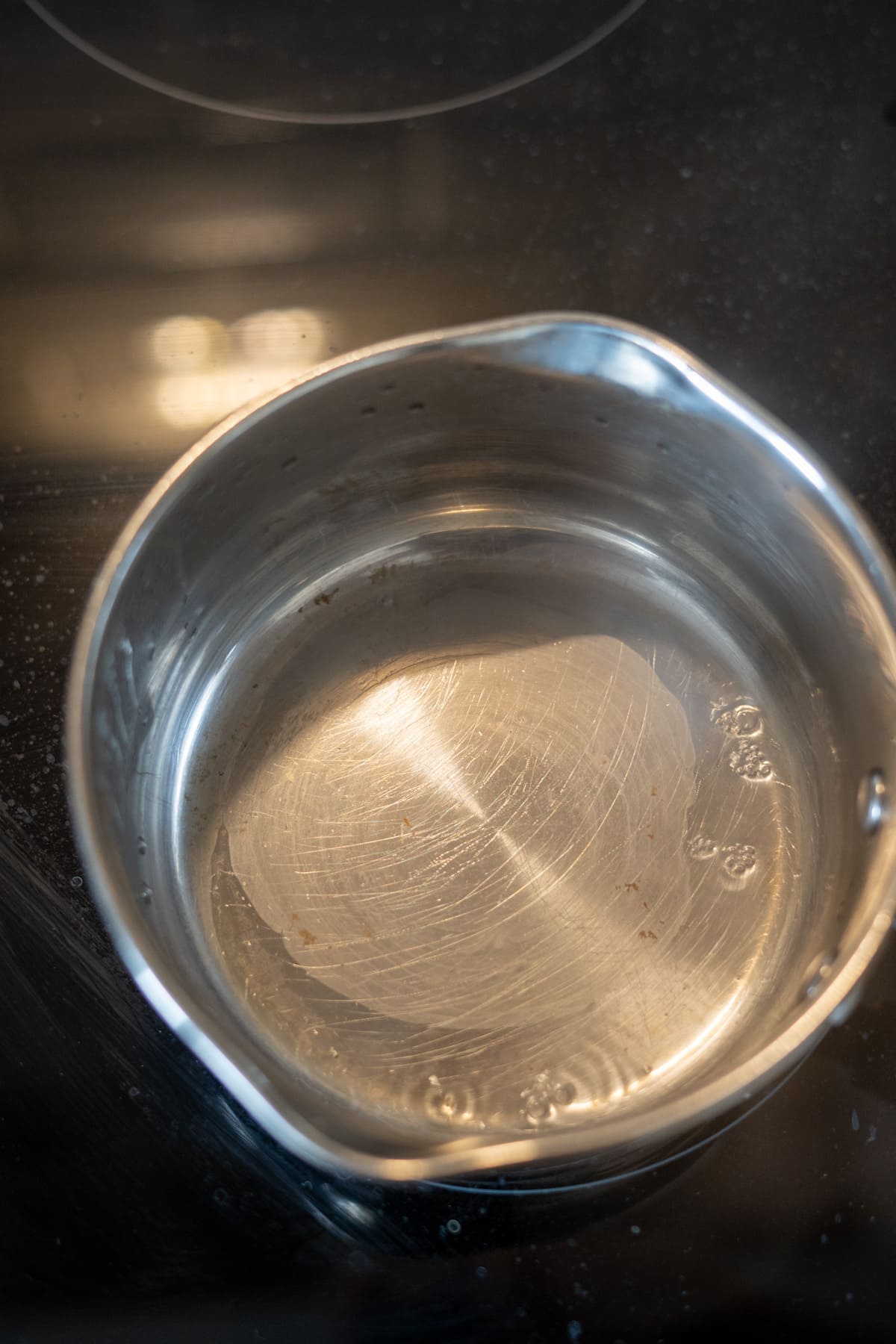 A stainless steel saucepan with a small amount of water inside is heating on a black electric hob, ready to help prepare scrambled eggs for dogs.