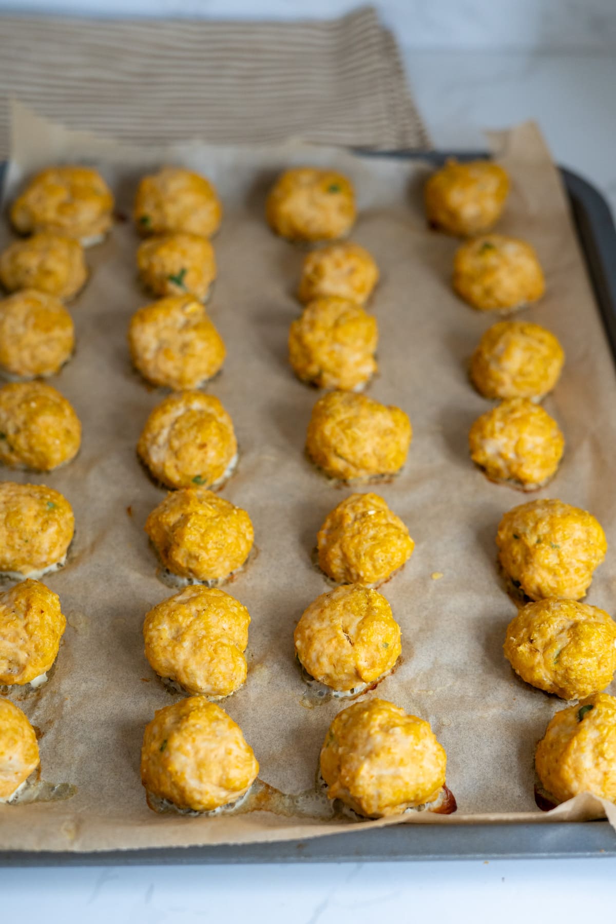 A baking tray lined with greaseproof paper holds several rows of evenly spaced, uncooked orange-tinted meatballs.