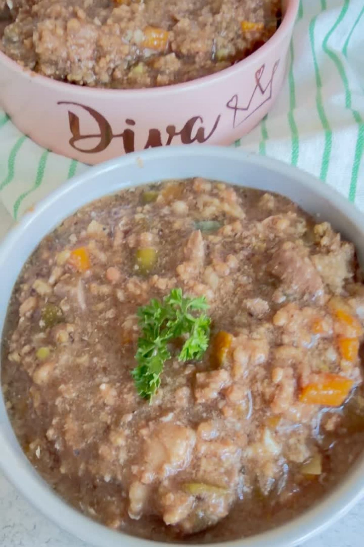 Two bowls of chunky stew with vegetables and meat are shown; one bowl is garnished with parsley and the other has “Diva” written on it, highlighting a delicious homemade Slow Cooker Beef Dog Food perfect for your furry friend.