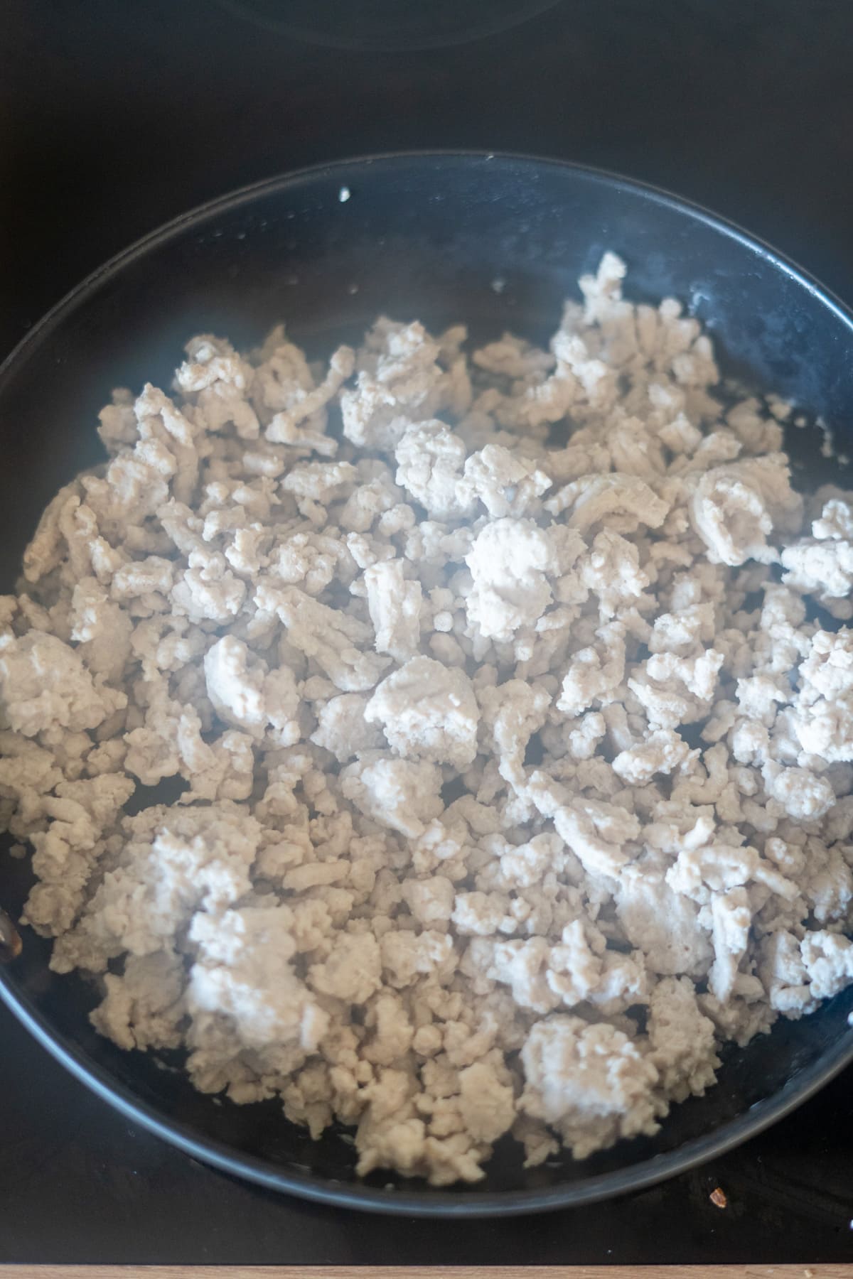 Cooked minced turkey in a black frying pan on a hob, with steam rising from the meat.