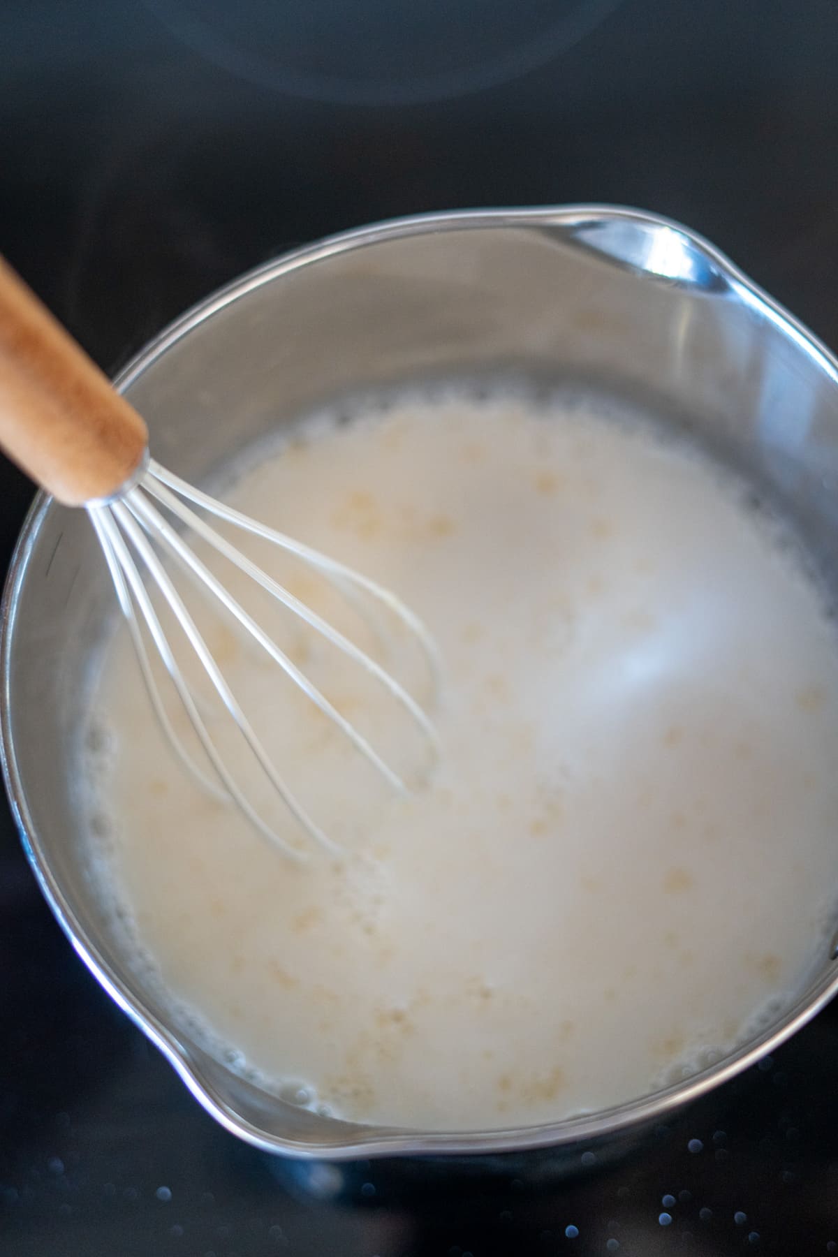 A whisk stirring a pot of goat’s milk on a hob, perfect for making nutritious bone broth gummies for dogs.
