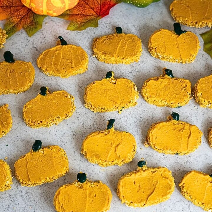 Pumpkin-shaped biscuits with orange icing and green stems are arranged on a grey surface.