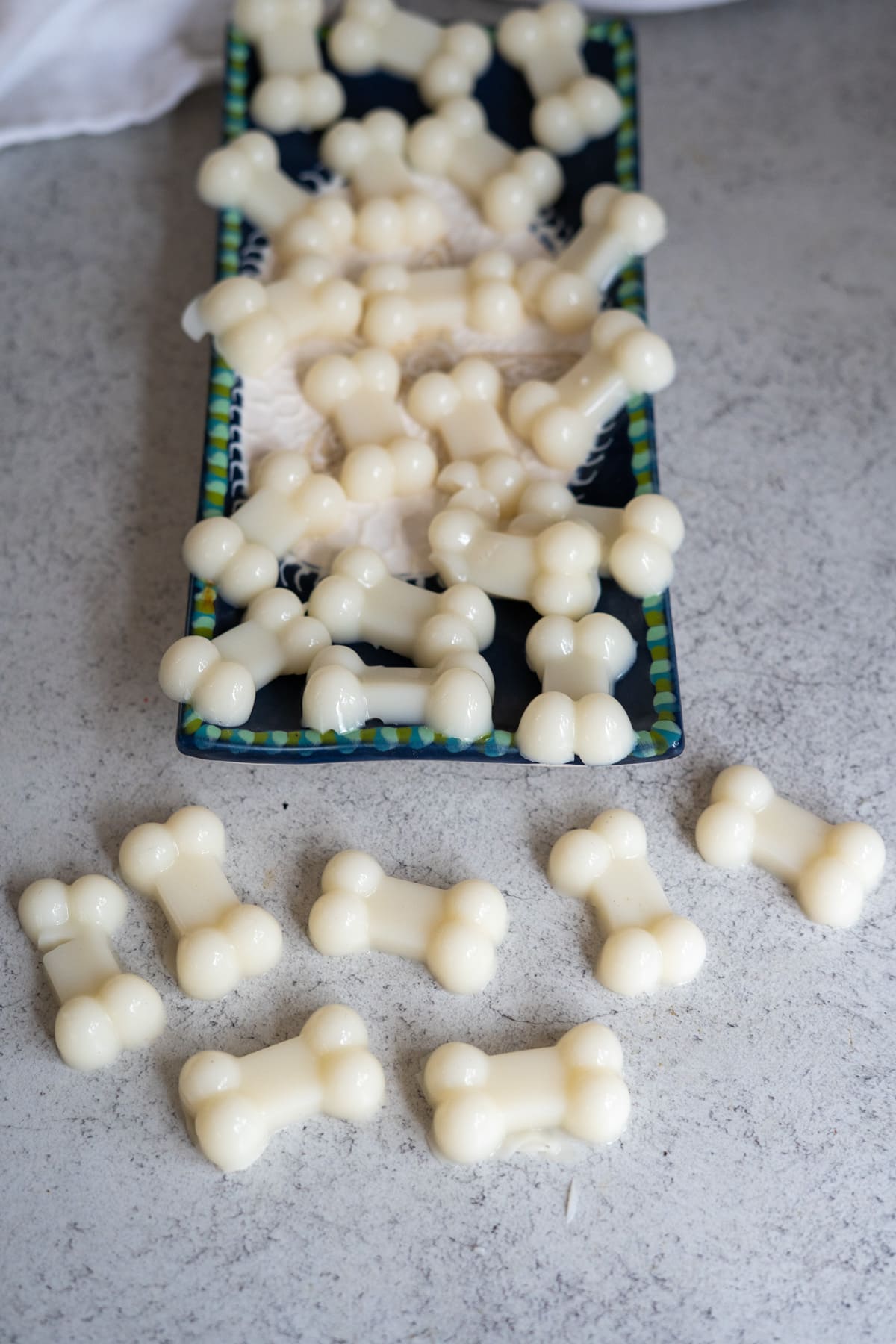 A tray and worktop with several white, bone-shaped dog treats, including goat’s milk and bone broth gummies for dogs, arranged neatly and scattered.