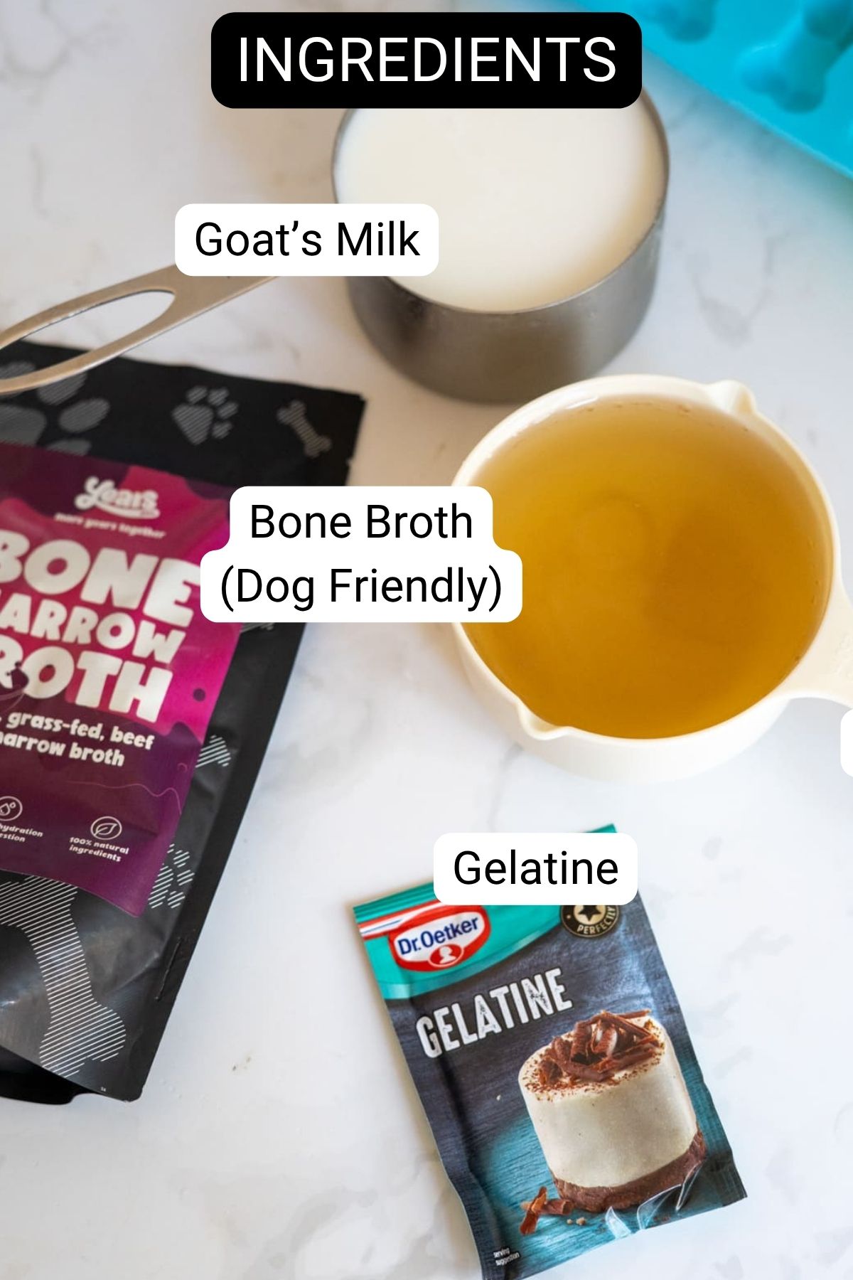 Goat’s milk in a bowl, dog-friendly bone broth in a measuring jug, a packet of gelatine, and a bag of bone broth are all arranged on a white worktop—everything you need to make goat’s milk and bone broth gummies for dogs.