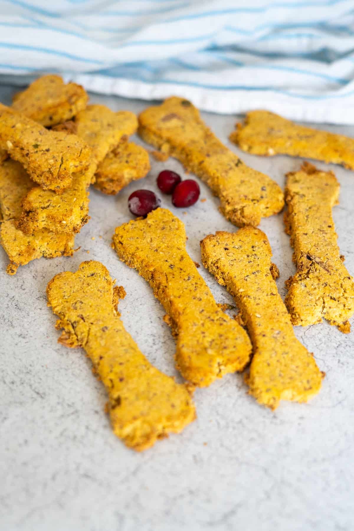 Bone-shaped Turkey Pumpkin Cranberry Dog Treats with three cranberries on a light grey surface and a blue and white striped cloth in the background.