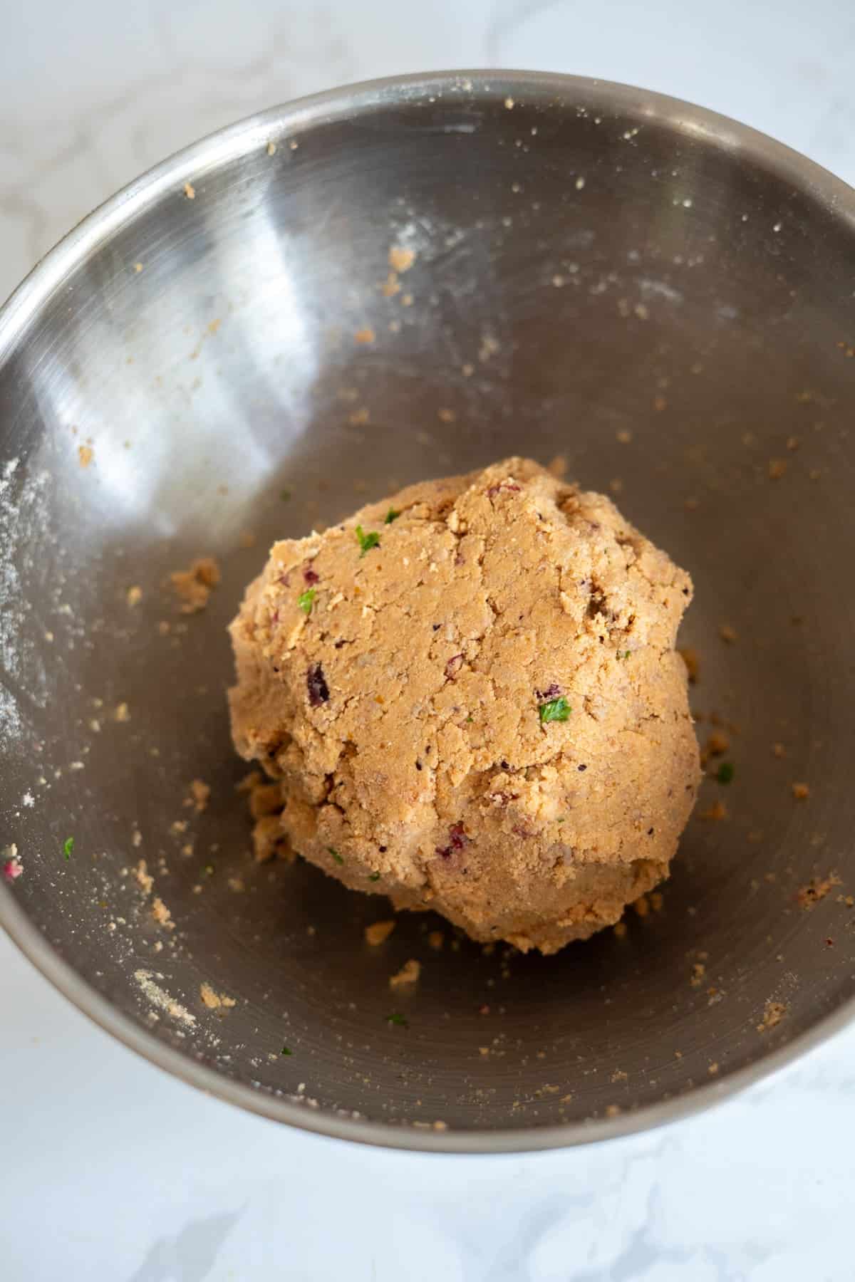 A ball of uncooked Turkey Pumpkin Cranberry Dog Treats dough with herbs and mix-ins sits in a large metal mixing bowl on a light-coloured surface.
